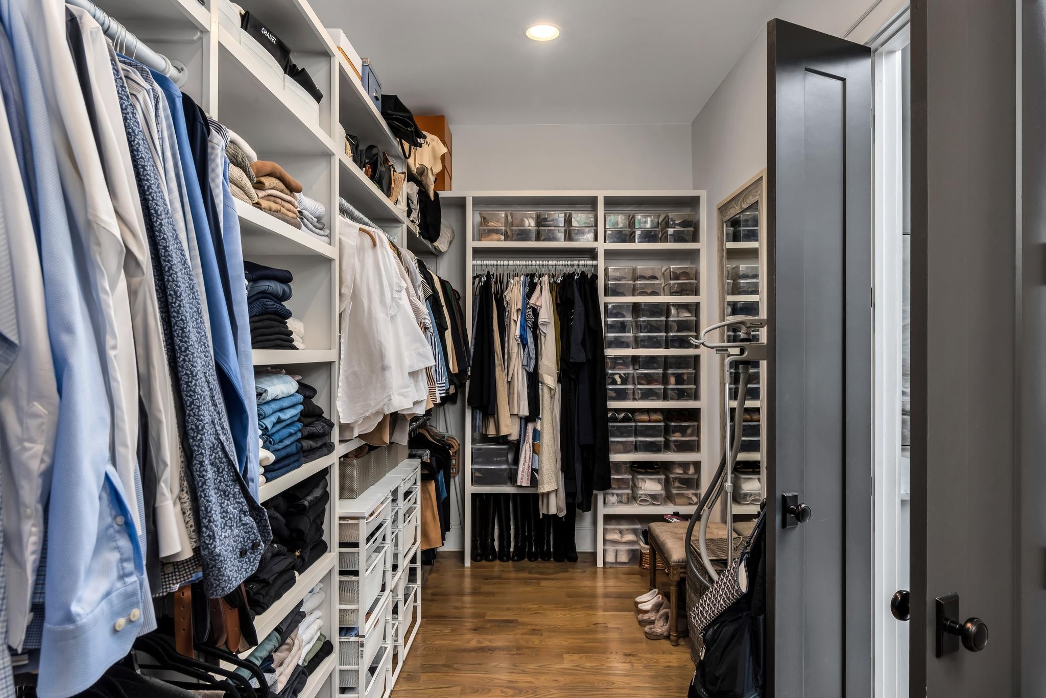 Walk-in closet with built-in shelving, hanging clothes, clear shoe boxes, and hardwood flooring.