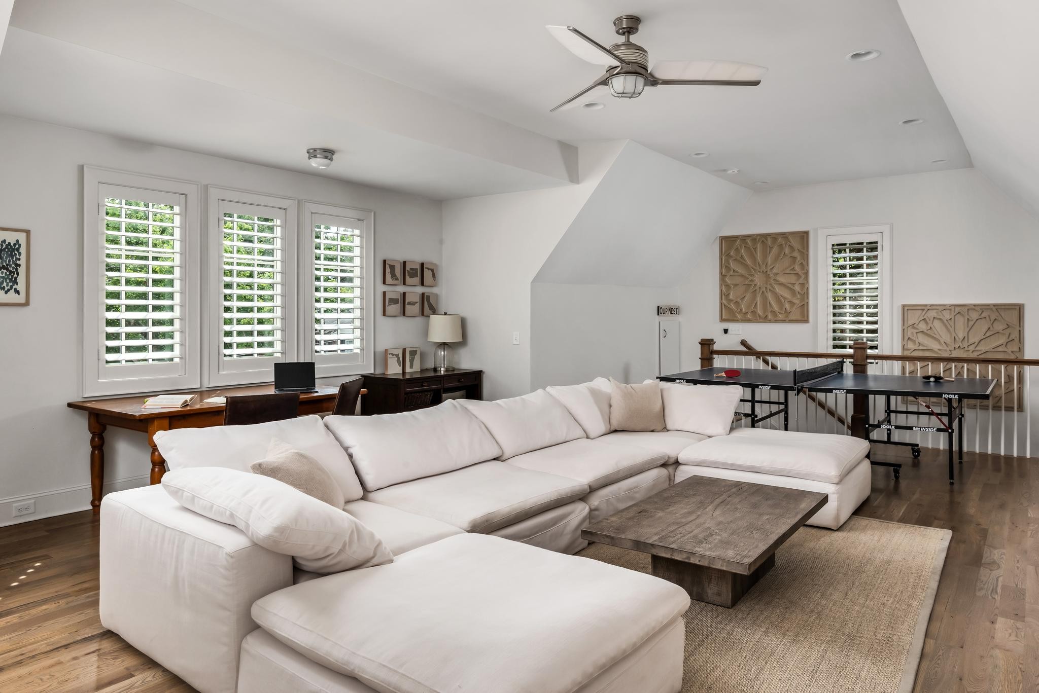 Living and recreation room with a white sectional sofa, shuttered windows, and a ping-pong table.
