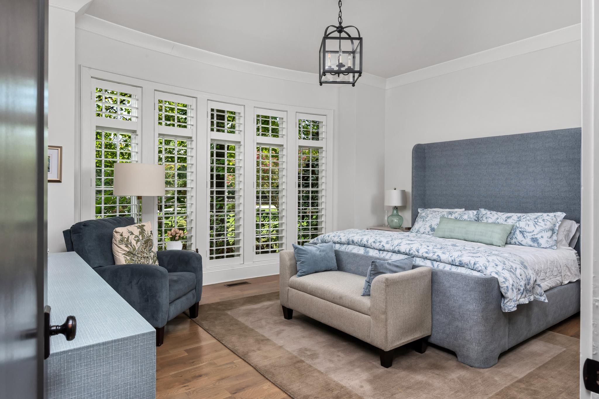 Bedroom with a gray upholstered bed, floral bedding, and tall plantation-shuttered windows.