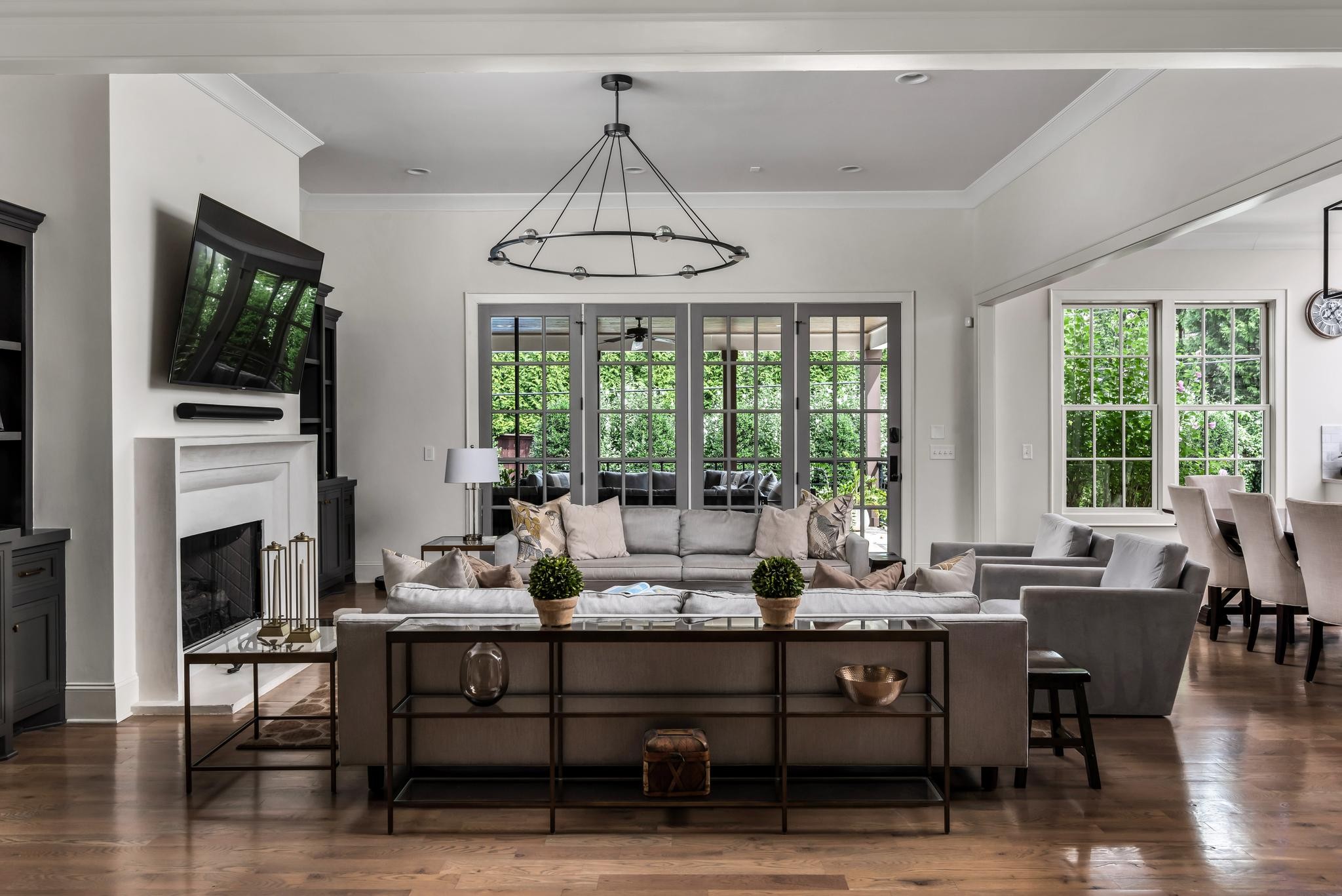 Living room with gray sofas, a white fireplace, and tall glass doors opening to a leafy patio.