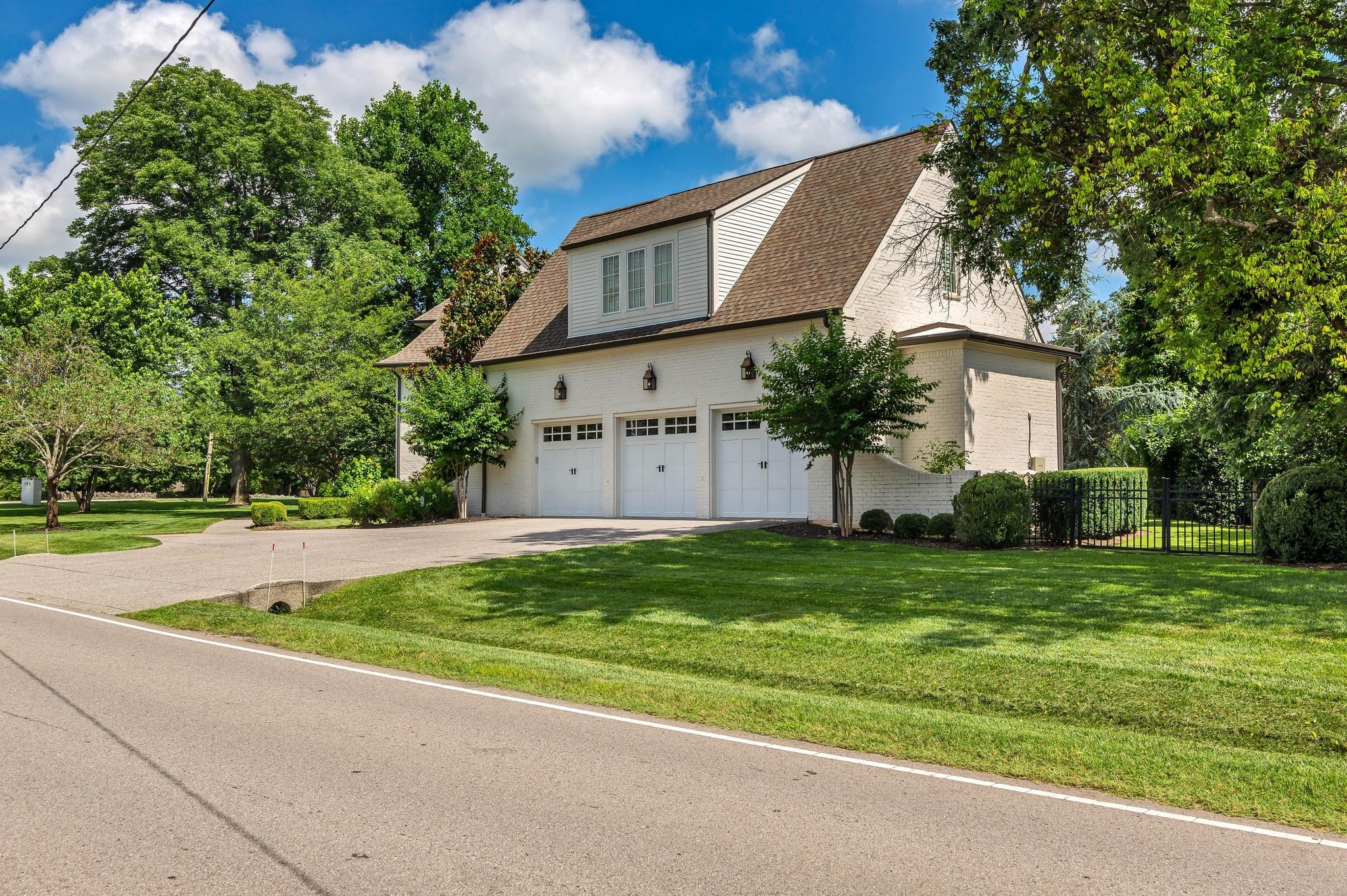 White brick home with three garage doors, a steep roof, and landscaped lawn.