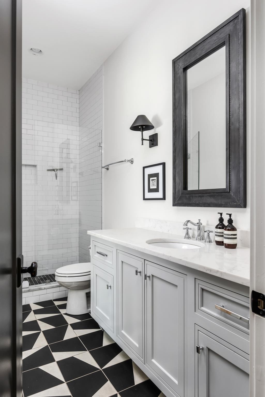 Bathroom with a white marble vanity, dark-framed mirror, subway-tile shower, and geometric black-and-white floor.
