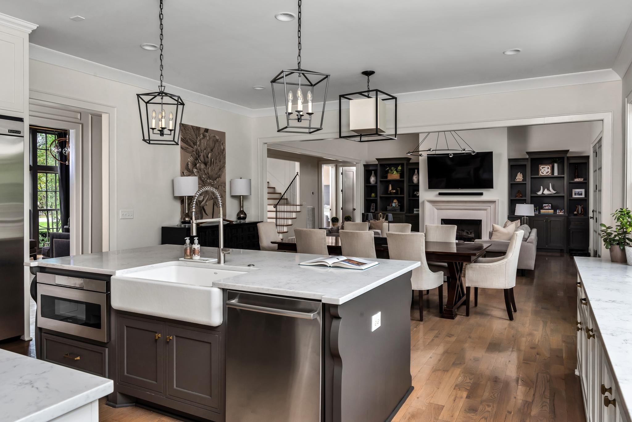 Open-plan kitchen with marble island and farmhouse sink, dining area, and fireplace beyond.