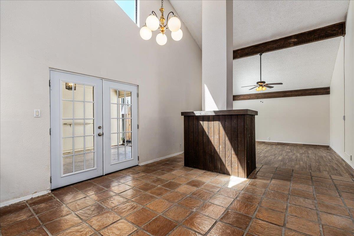 Vacant vaulted interior with French doors, terracotta tile, and dark exposed ceiling beams.