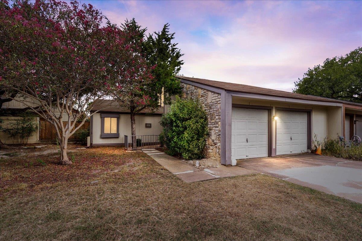Single-story home with a stone facade, two-car garage, and pink-flowering tree.