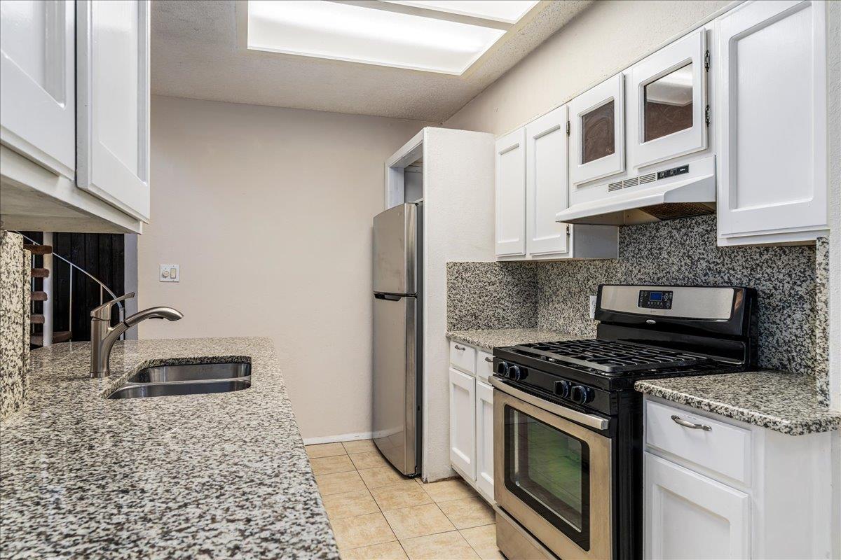 Kitchen with speckled granite counters, white cabinets, a gas range, and a skylight.