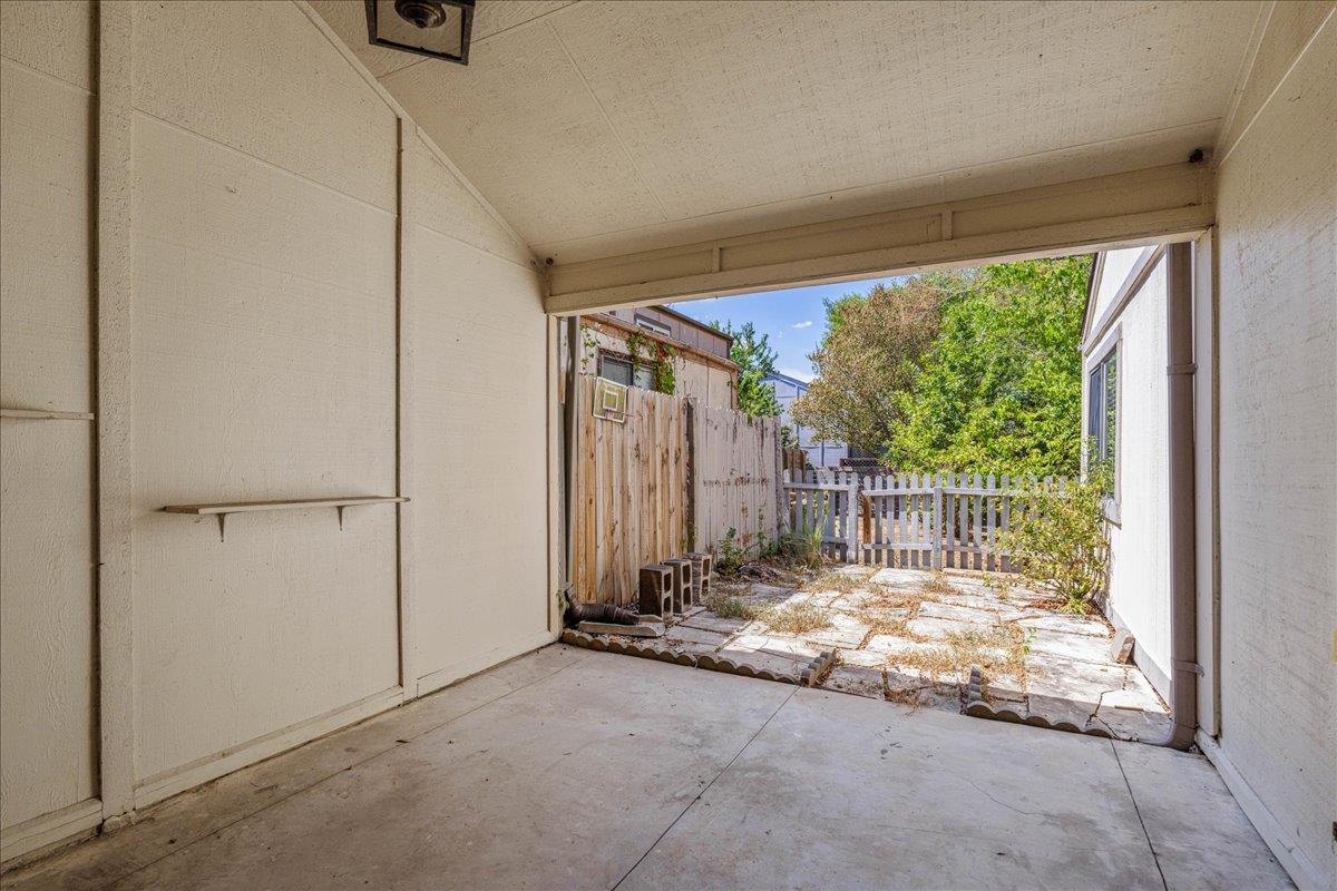 Covered patio overlooking a fenced, paved backyard with trees.