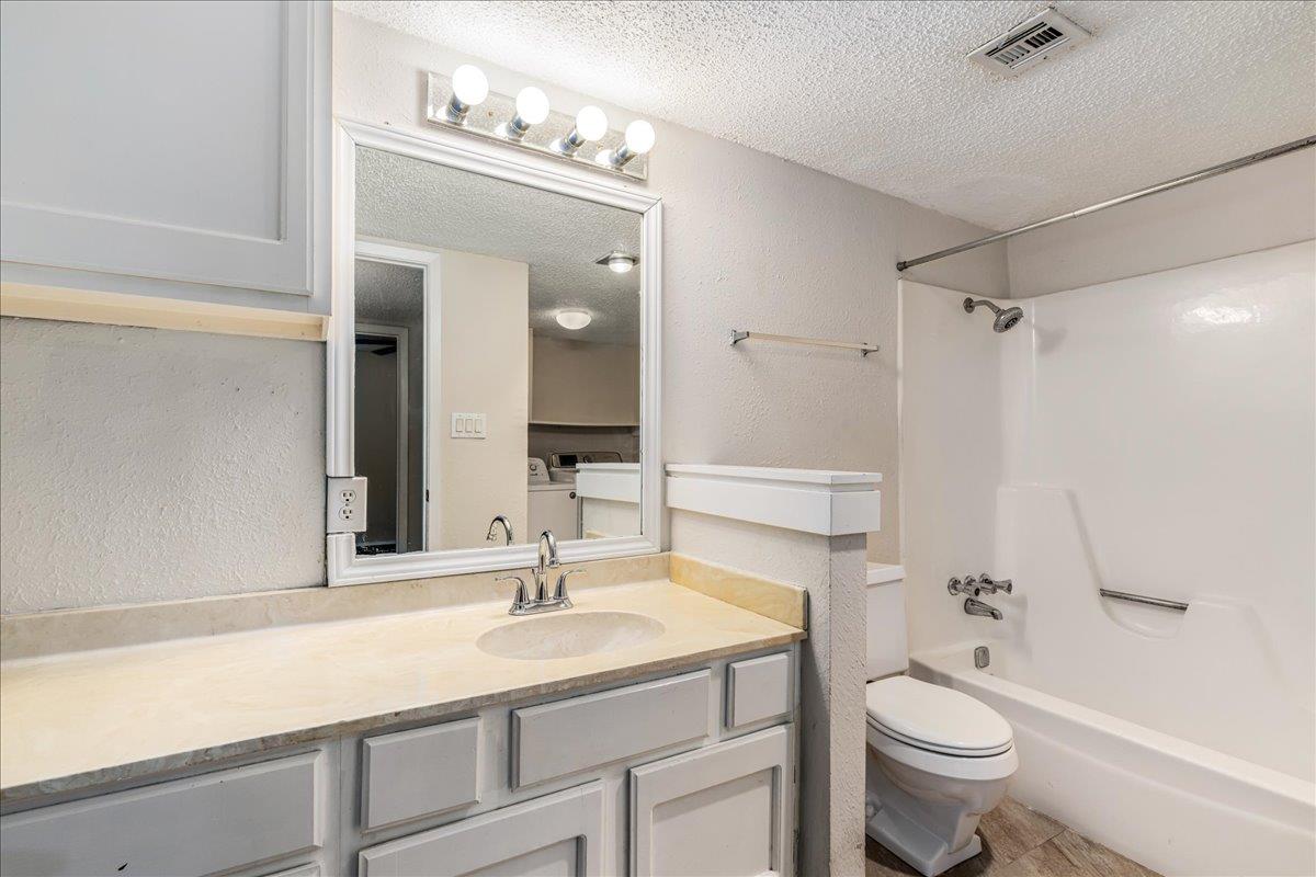 Bathroom with a long vanity, bright mirror lights, and a white tub-shower.