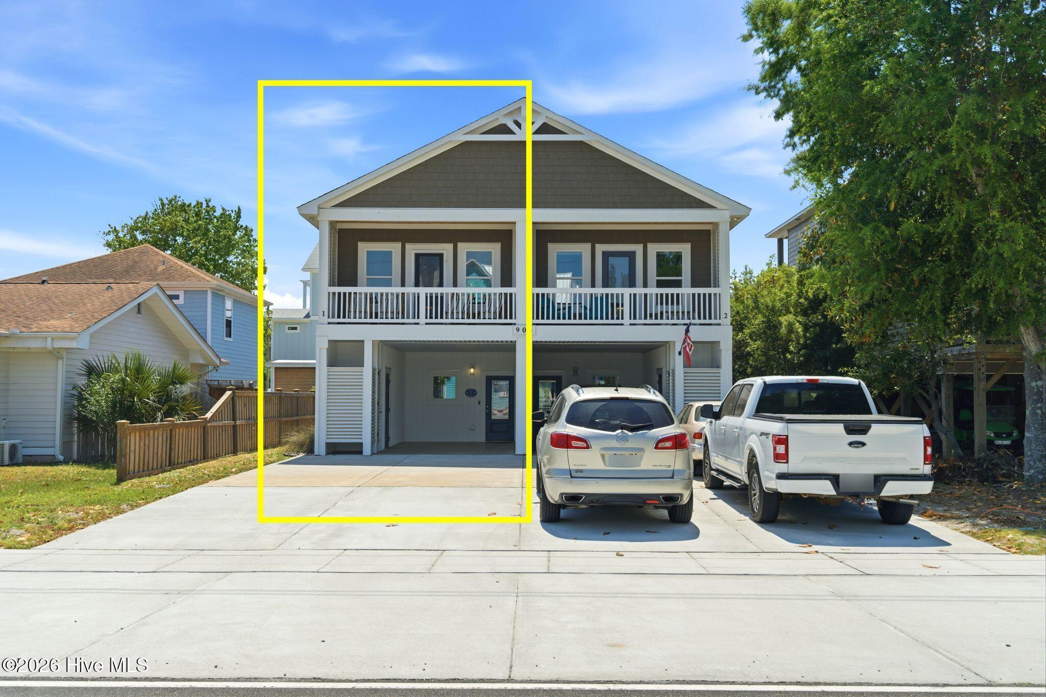 Raised two-unit home with porches; a yellow outline highlights the left unit beside a driveway with two vehicles.