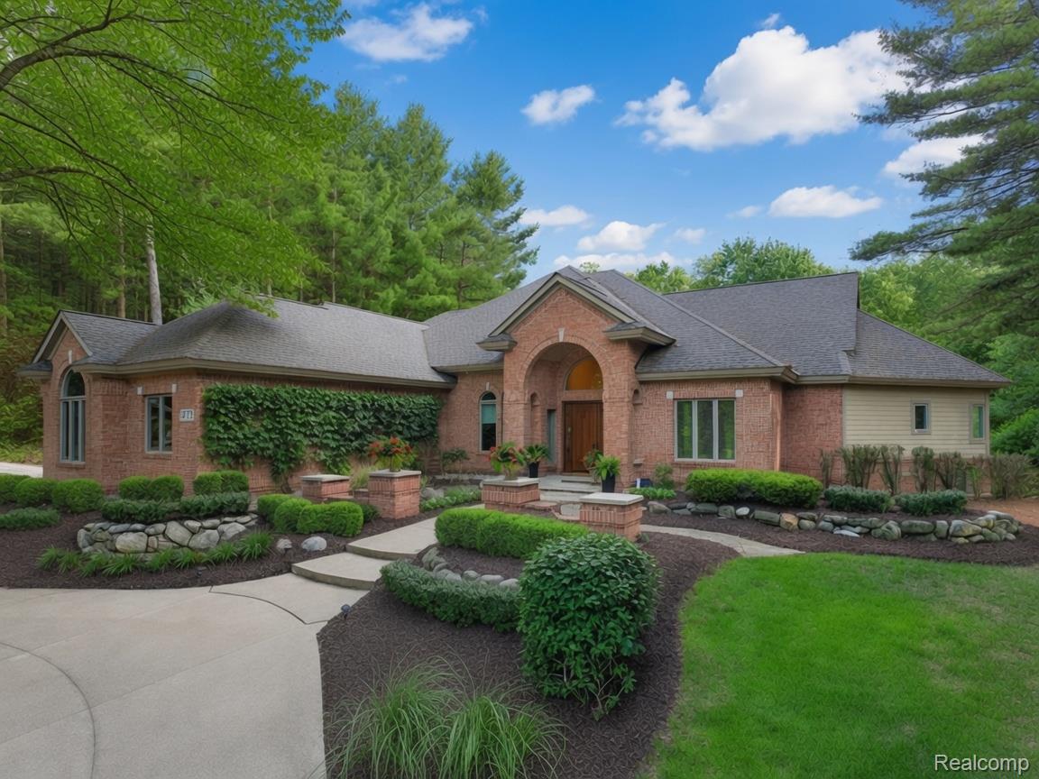Brick home with an arched entry, landscaped garden beds, and a curved driveway beneath mature trees.