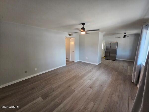 Vacant open-plan living and dining area with wood-look floors, two ceiling fans, and a stainless-steel refrigerator.