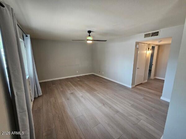 Empty room with wood-look flooring, a ceiling fan, and curtained windows.