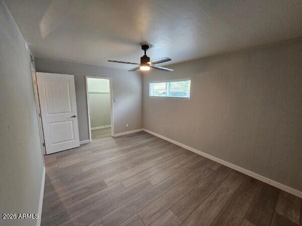 Empty bedroom with wood-look flooring, ceiling fan, and a small window.