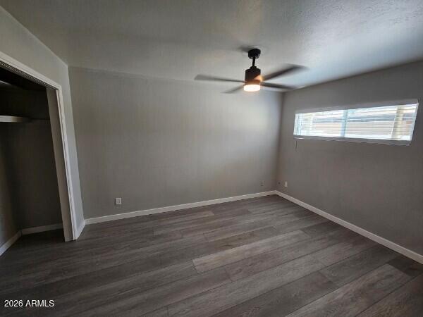 Empty bedroom with gray plank flooring, a ceiling fan, and a narrow window with blinds.