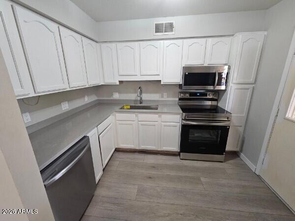 Kitchen with white cabinets, gray countertops, stainless-steel appliances, and gray wood-look flooring.