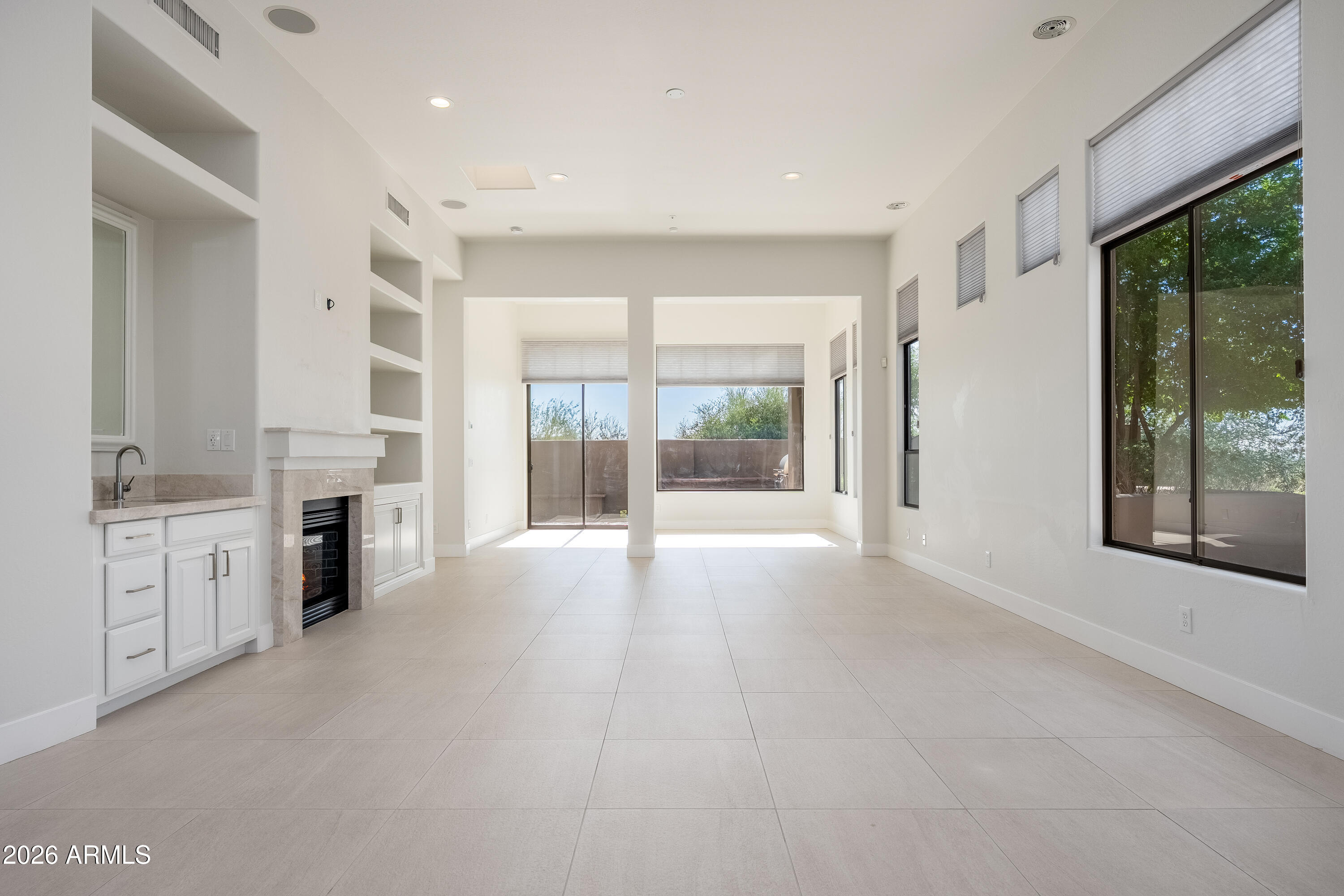 Bright vacant living room with tile floors, built-in fireplace, and large shaded windows.