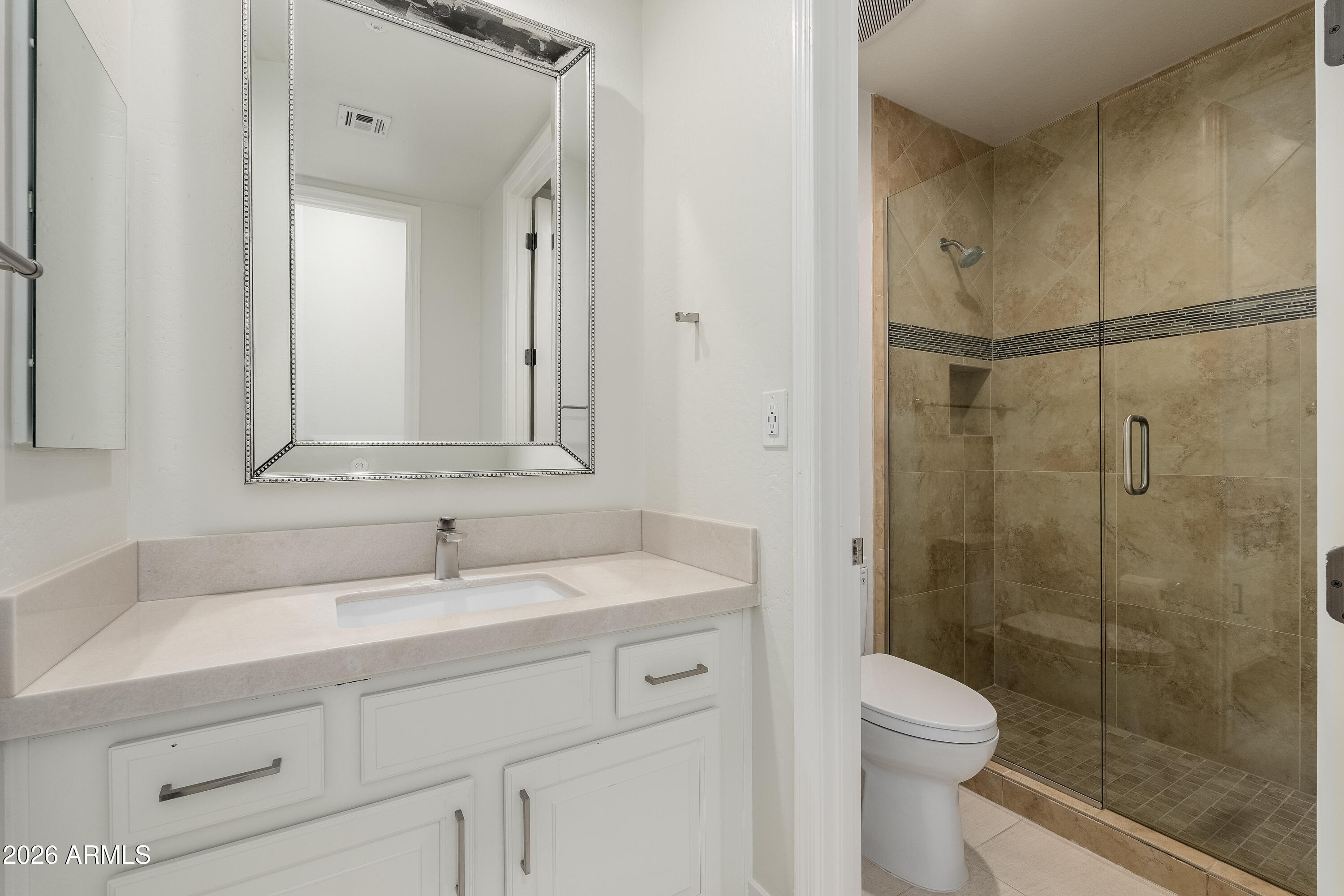 Bathroom with a white vanity and a tan-tiled glass shower.