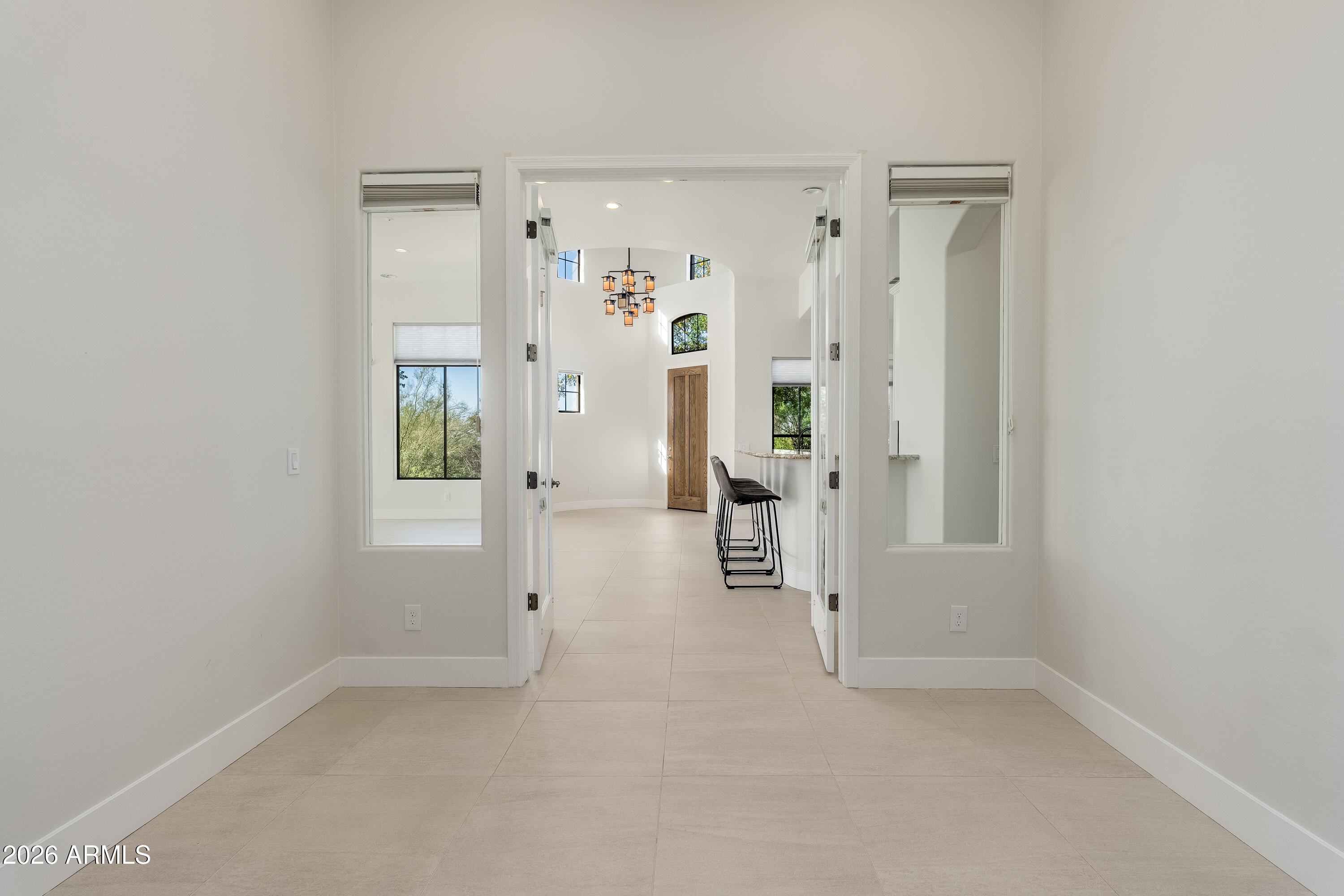 Foyer with tiled floors, a tall ceiling, geometric chandelier, wood entry door, and kitchen bar stools.