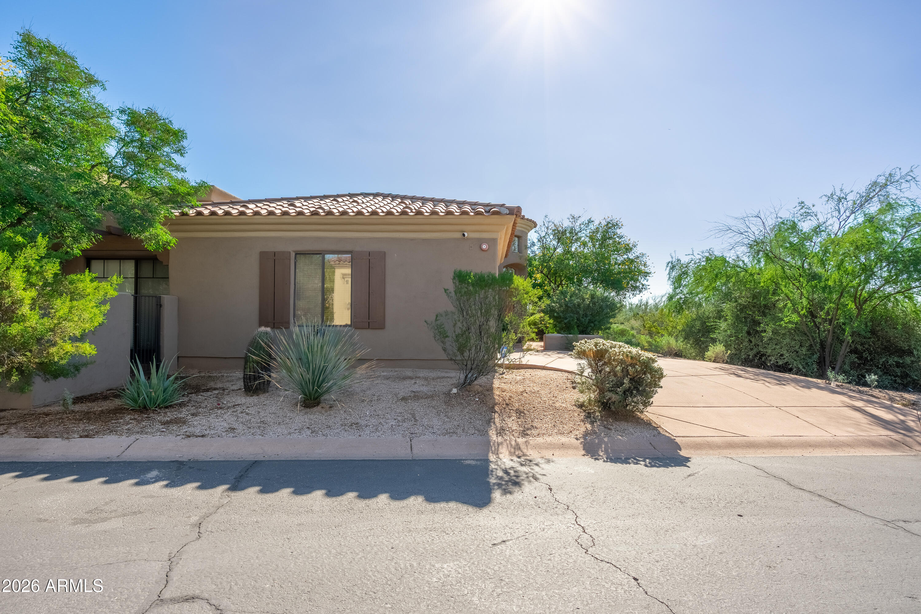 Tan stucco home with a tile roof, desert landscaping, and a paved driveway.