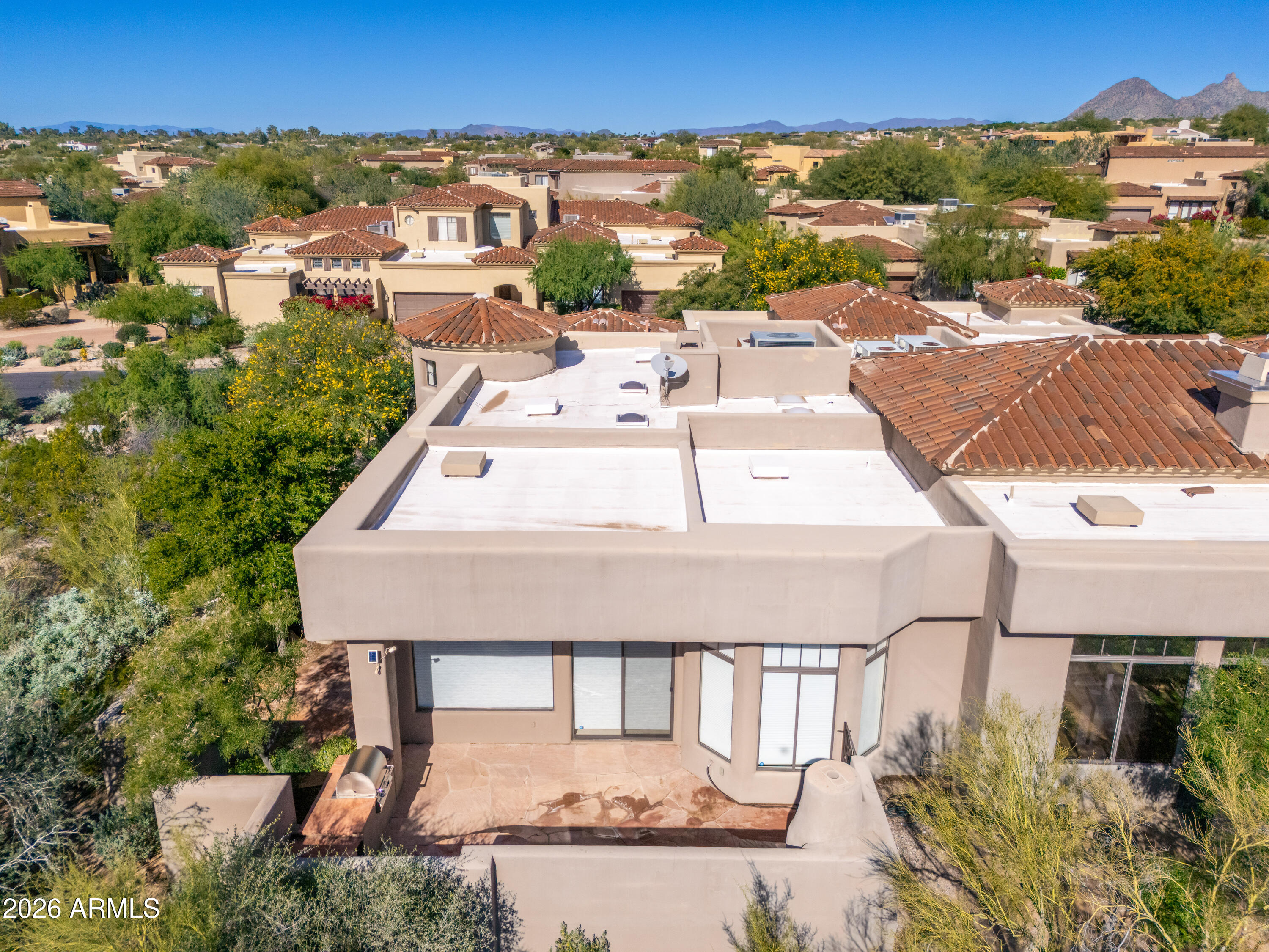 Aerial view of a stucco home with terracotta roof sections, desert landscaping, and mountains beyond.