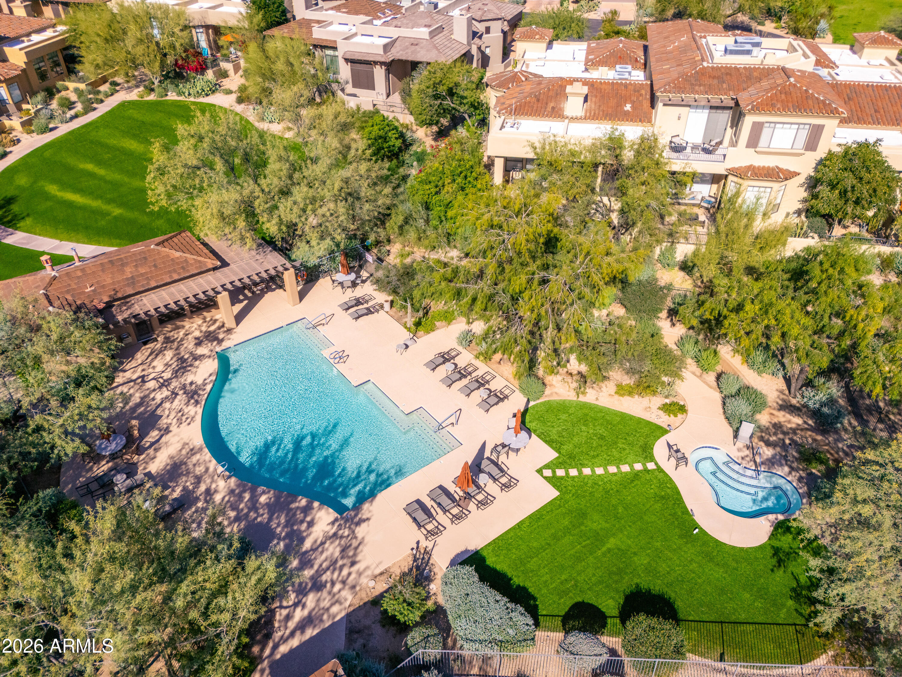 Aerial view of a community pool and spa beside landscaped lawns and homes.