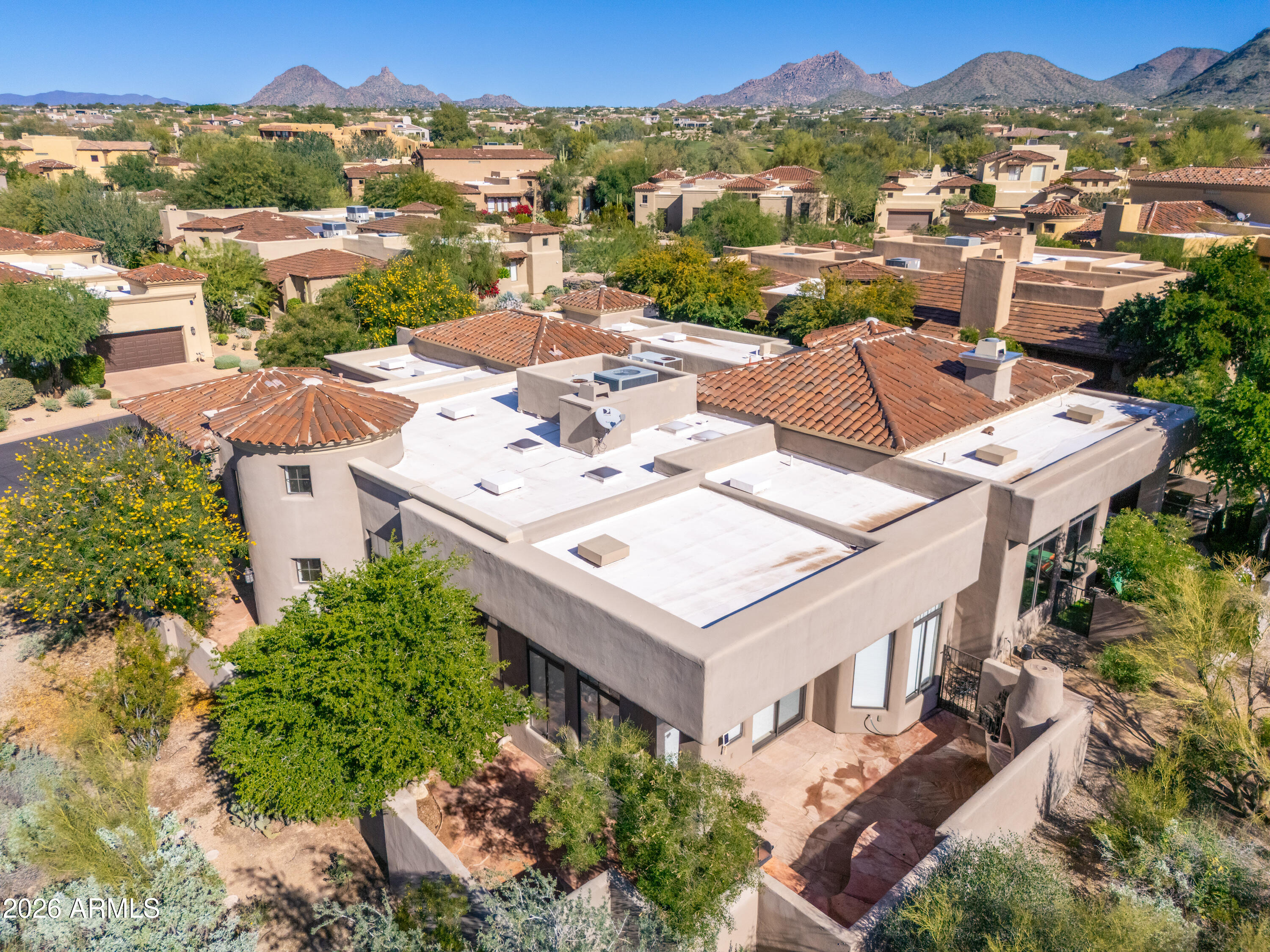 Aerial view of a desert home with terracotta roofs, landscaped yard, and mountain backdrop.