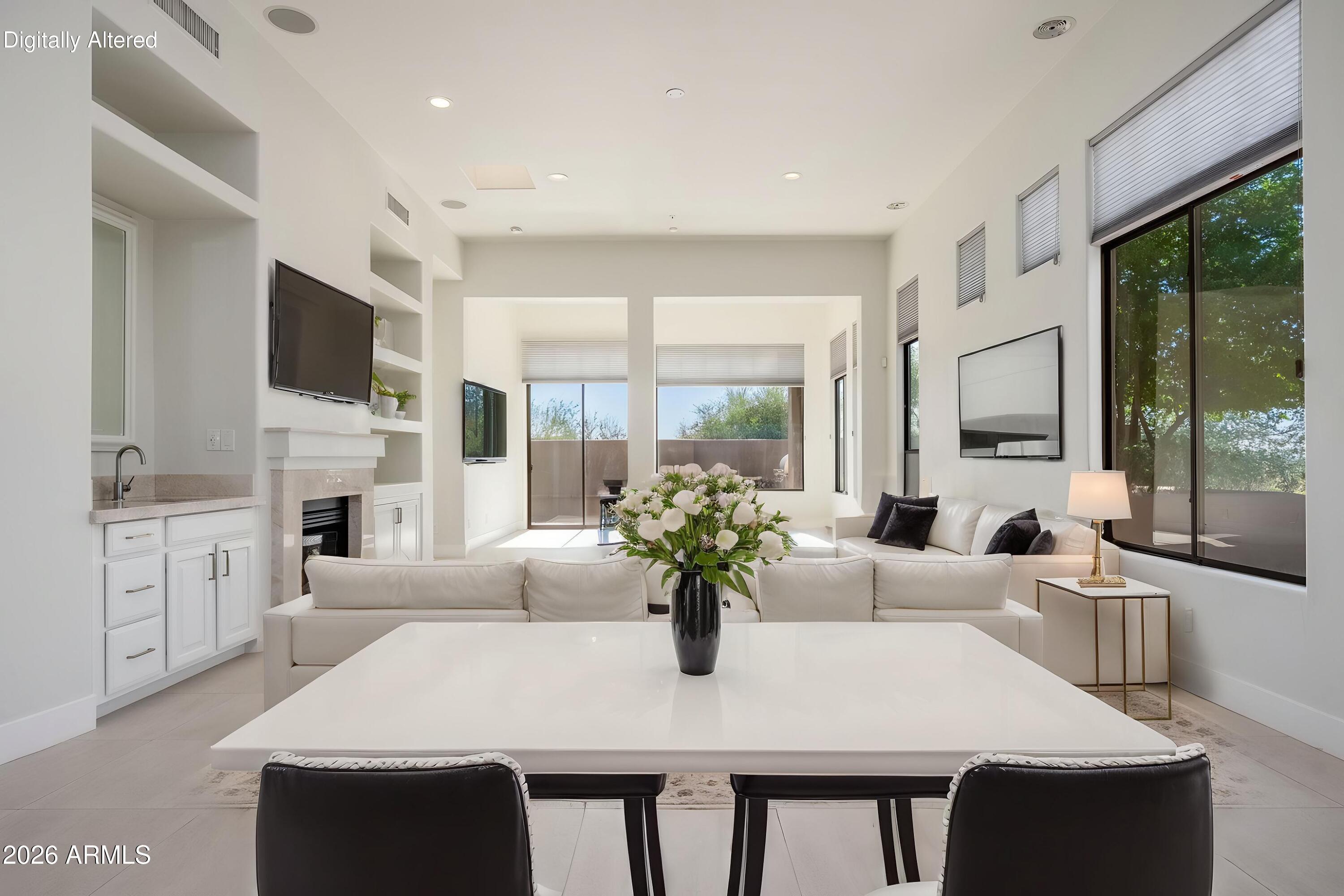 Living room with white sofas, fireplace, built-in television shelving, and large windows overlooking trees.
