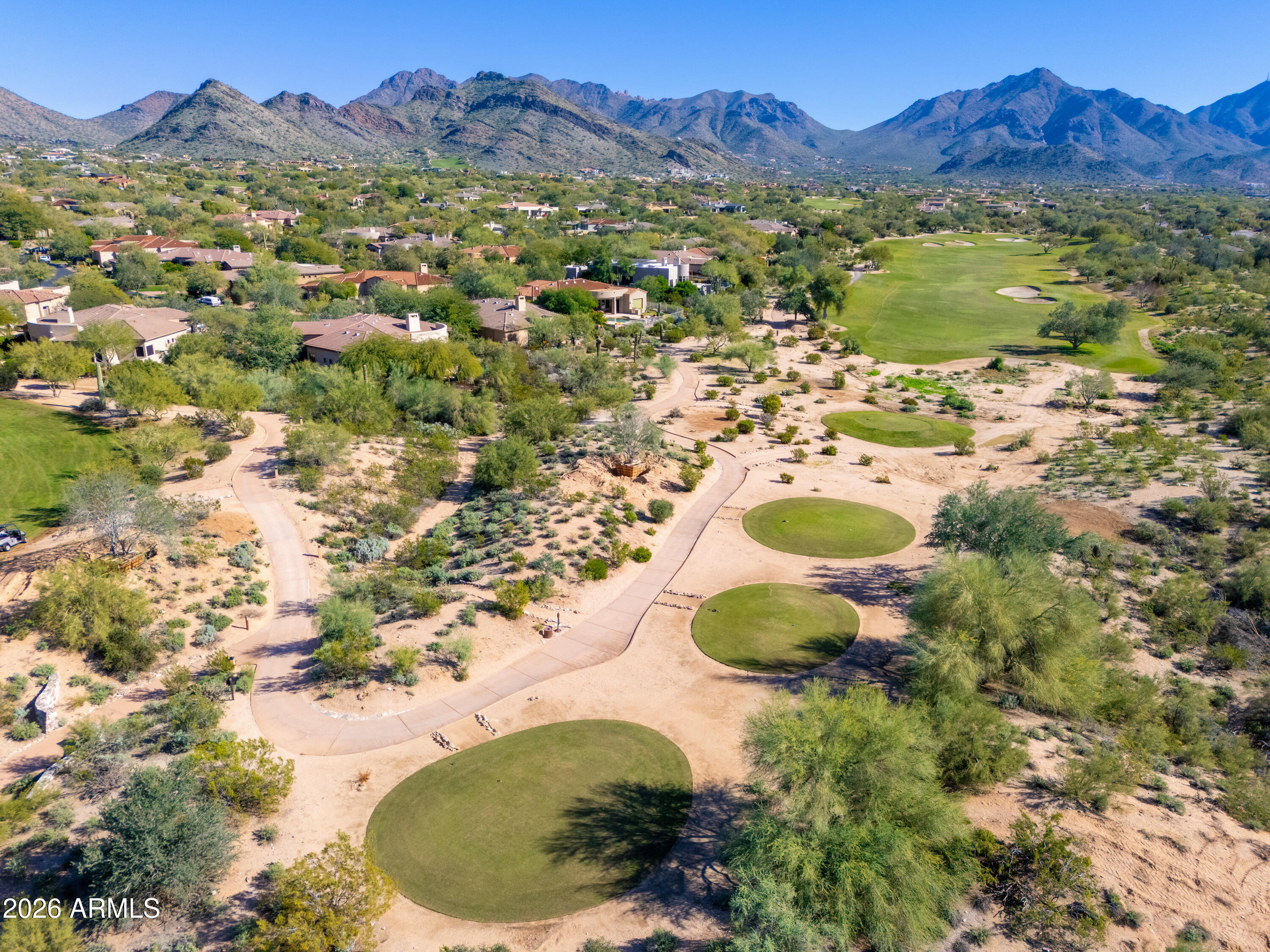Aerial view of desert homes beside a golf course, with winding paths and mountains beyond.