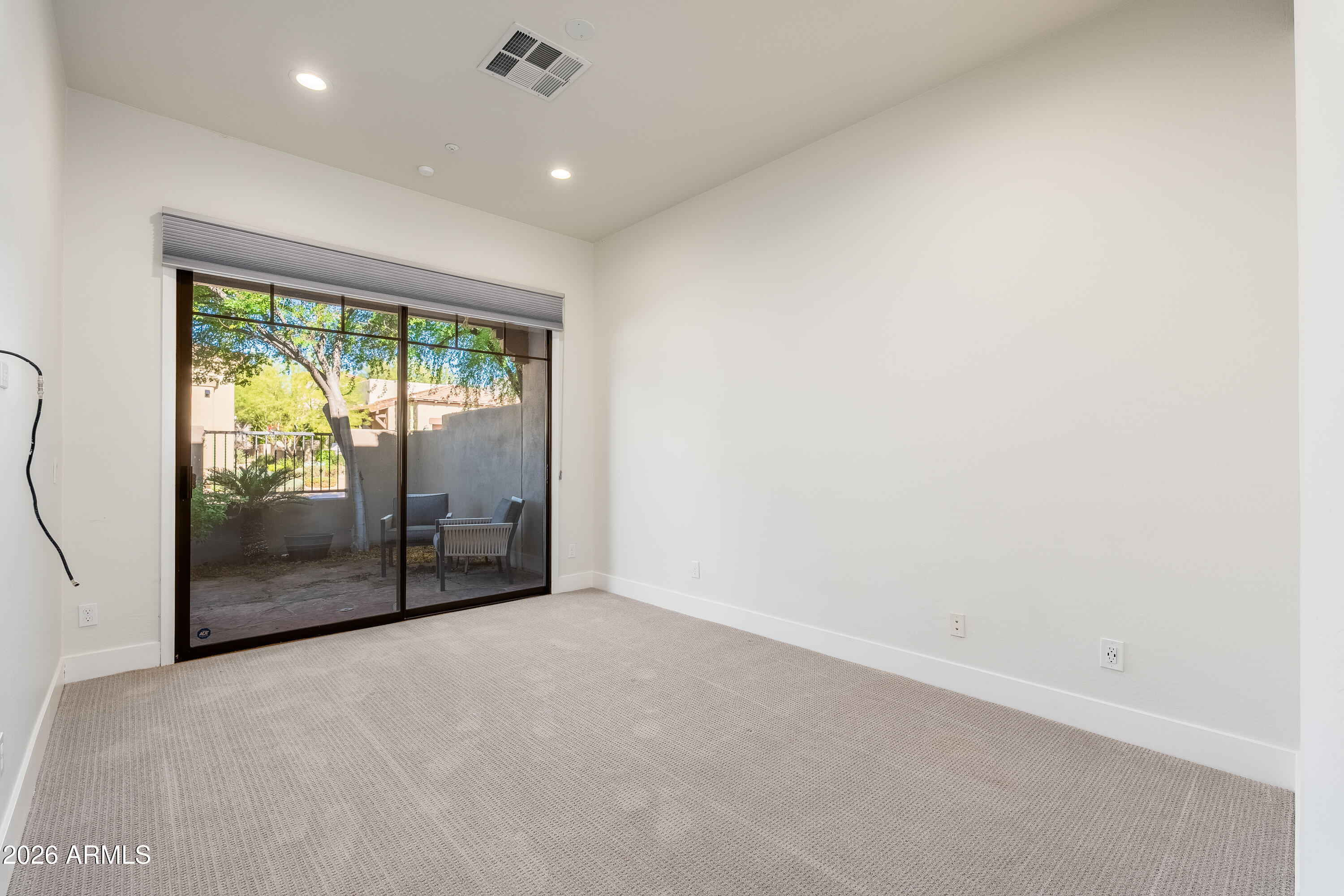 Empty carpeted room with a sliding glass door opening onto a tree-shaded patio.