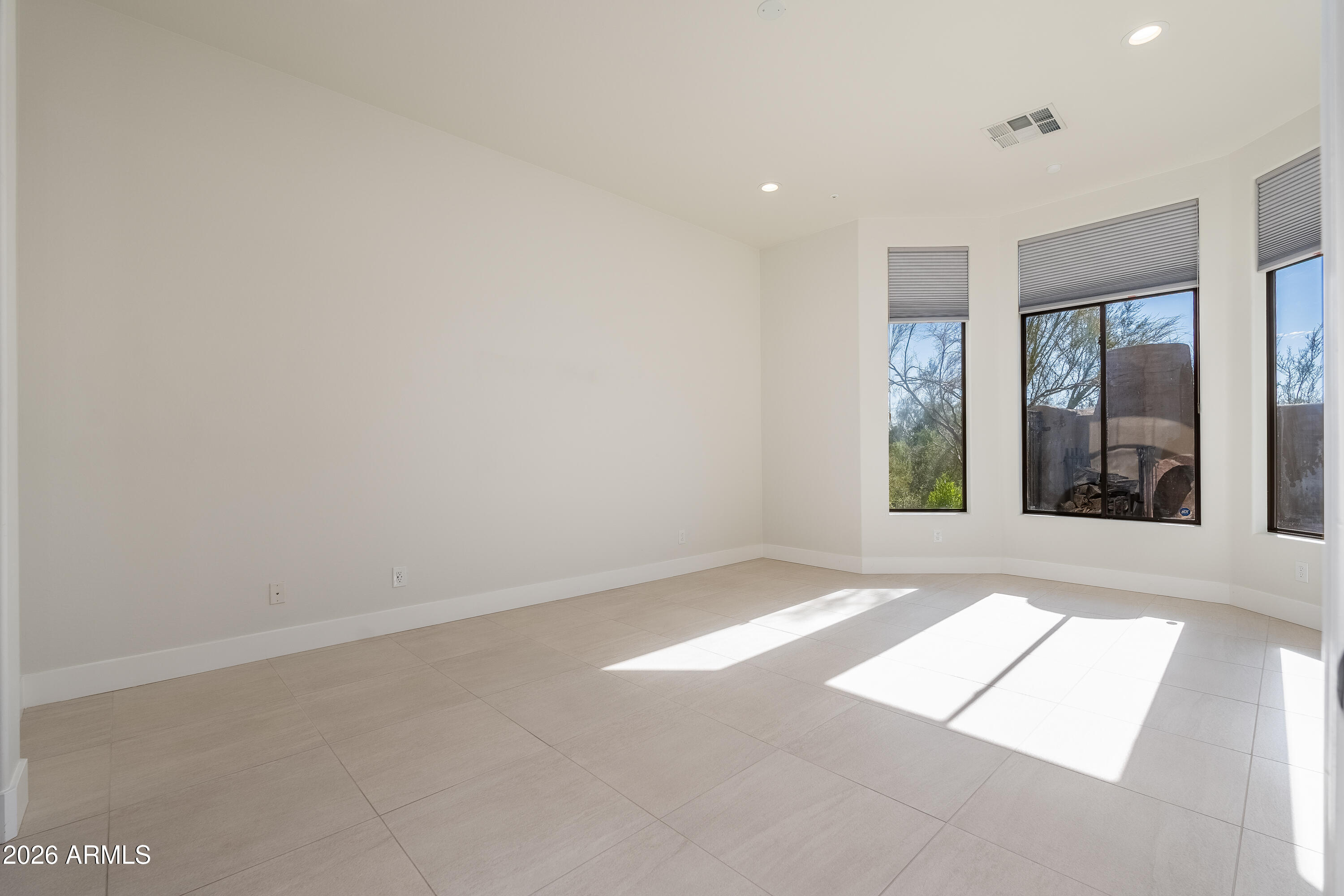 Vacant room with large tiled floors, tall windows, and sunlight streaming through gray blinds.