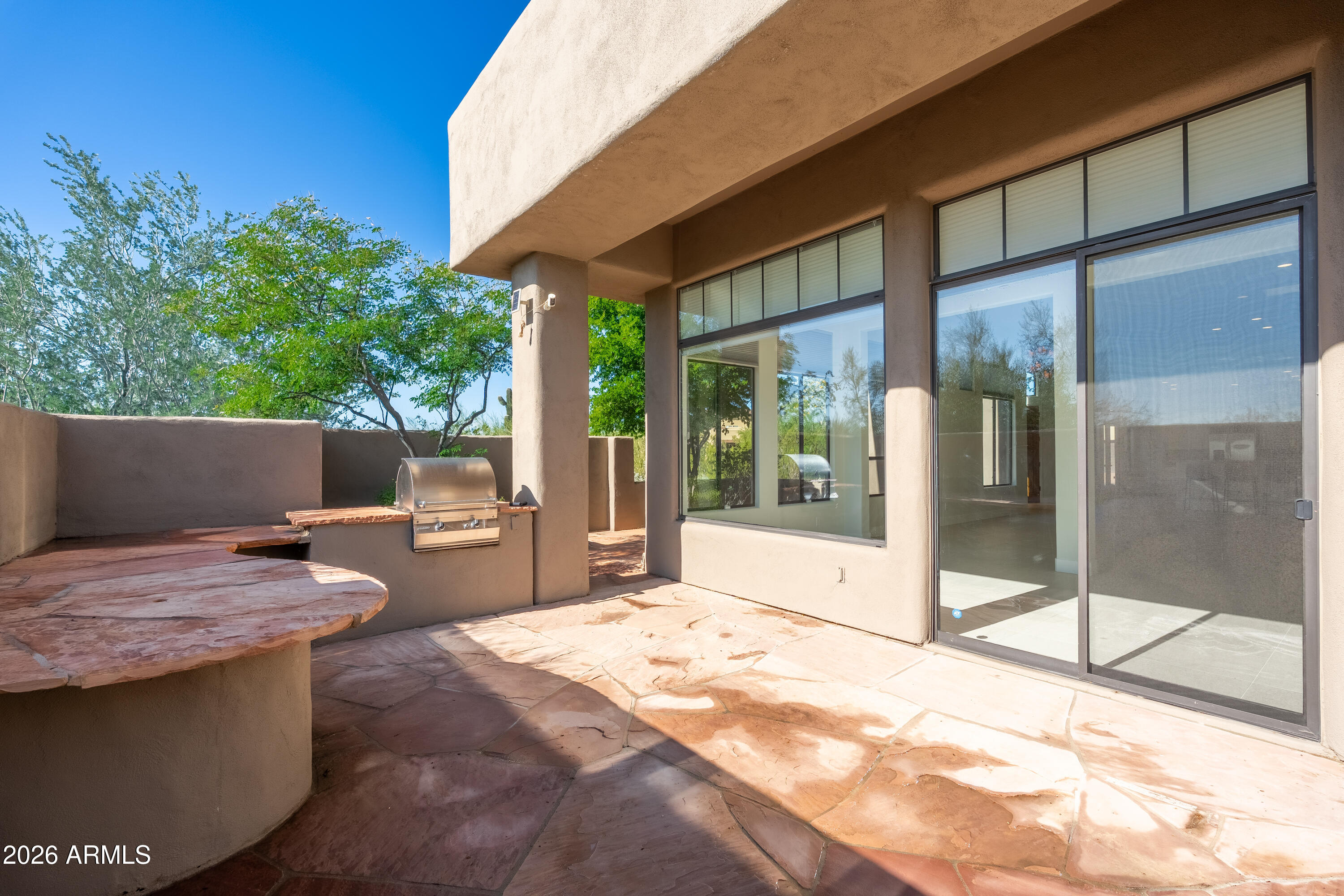 Stone patio with a built-in stainless steel grill and large sliding glass doors.