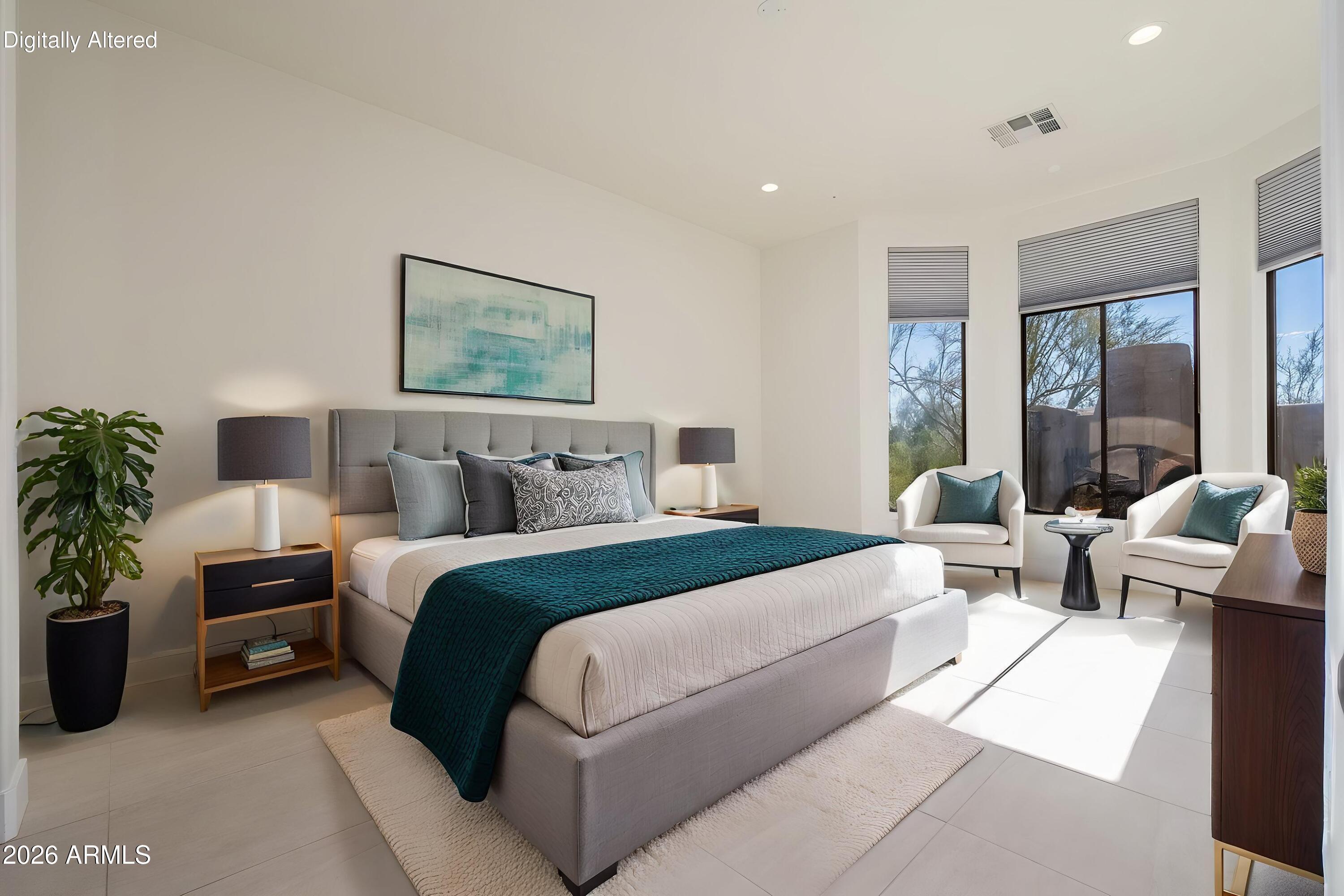 Furnished bedroom with a gray bed, teal coverlet, and two armchairs beside tall windows.