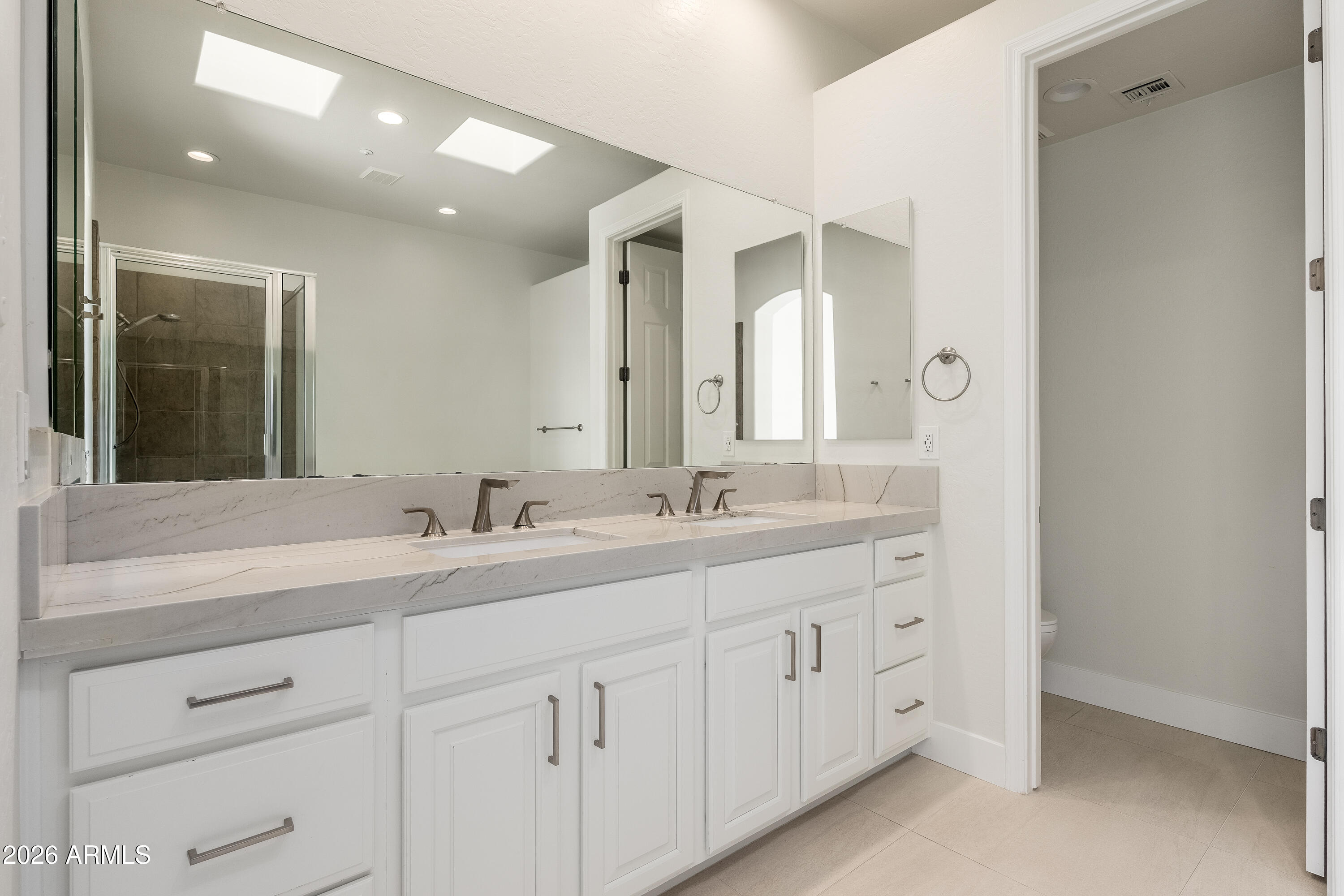 Bathroom with a white double vanity, veined stone counters, large mirrors, and glass-enclosed shower.