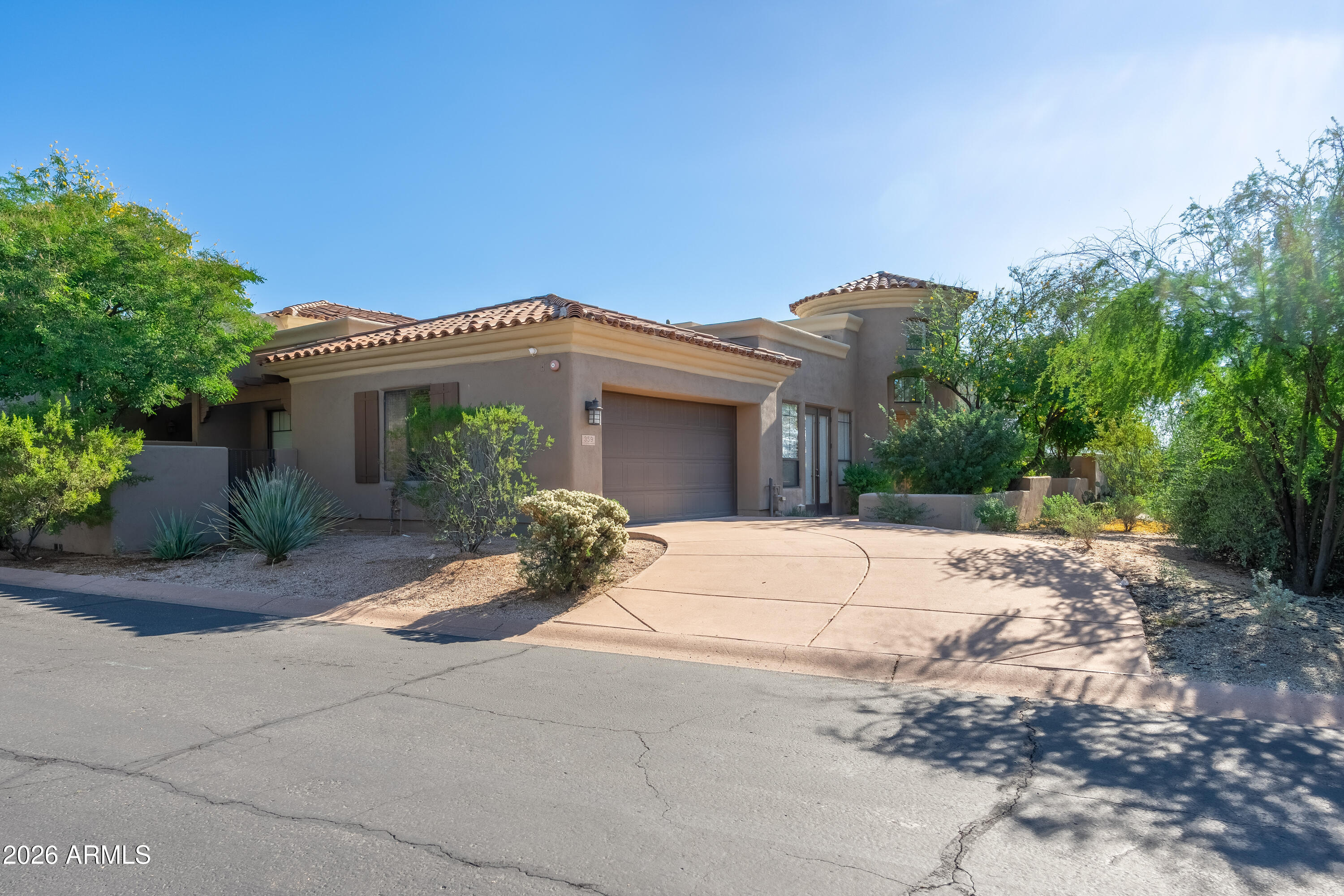Stucco home with a tiled roof, attached garage, and curved driveway amid desert landscaping.