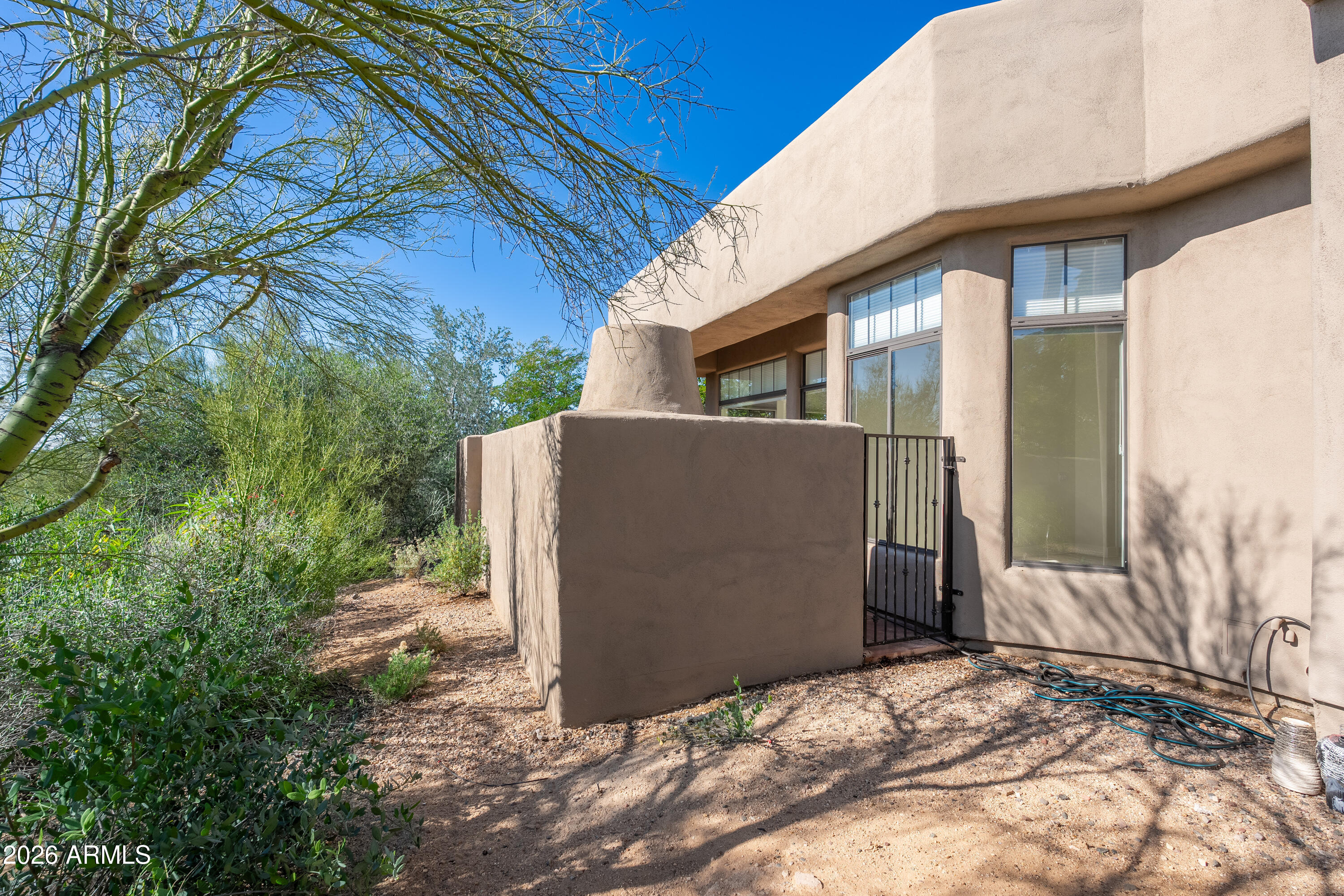 Tan stucco home exterior with a gated patio and desert landscaping.
