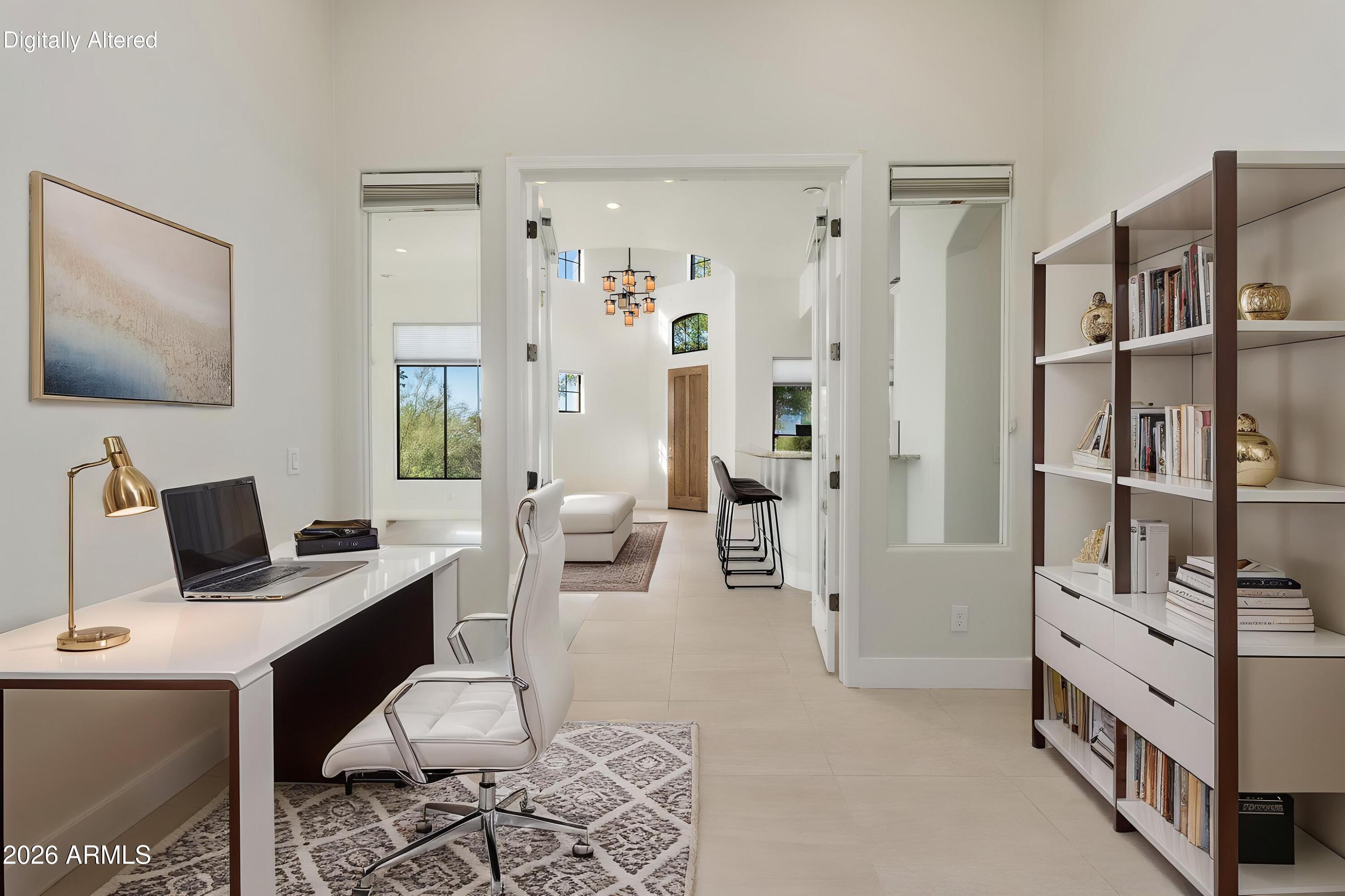 Staged home office with a white desk and built-in bookcase, opening onto a bright living area.