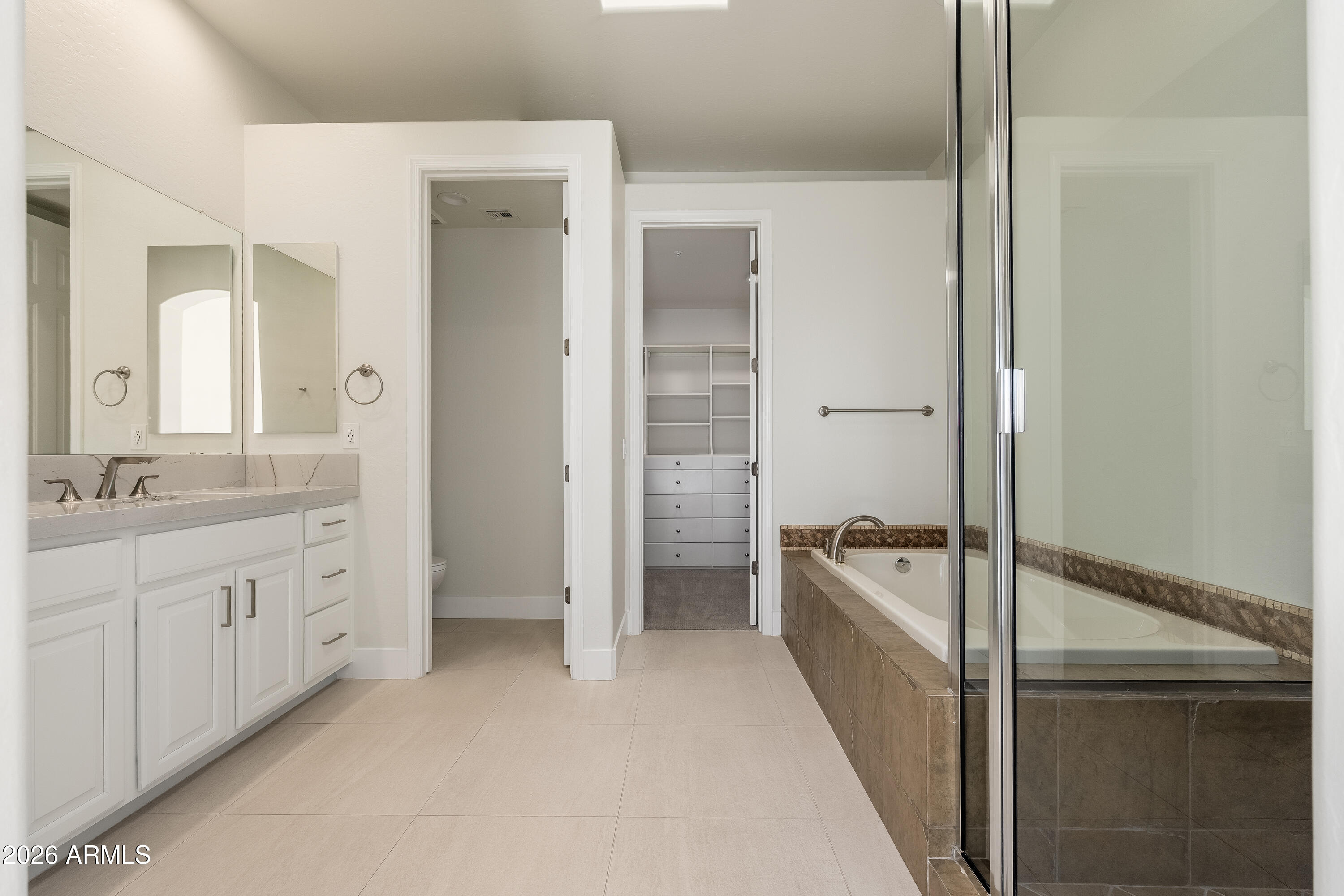 Primary bathroom with a white double vanity, glass-enclosed soaking tub, and walk-in closet.