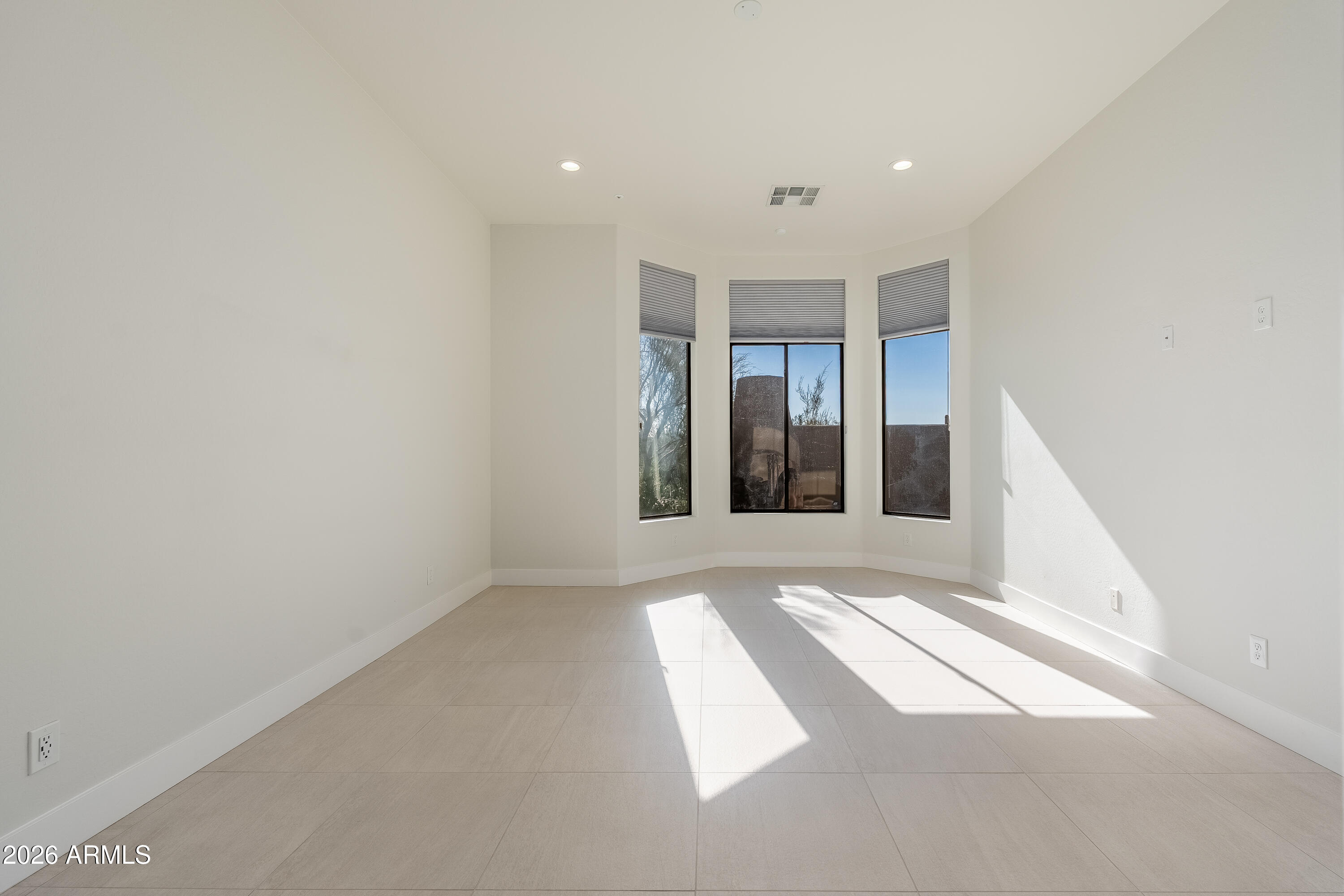 Empty room with tiled floors and three tall bay windows casting sunlight across the floor.