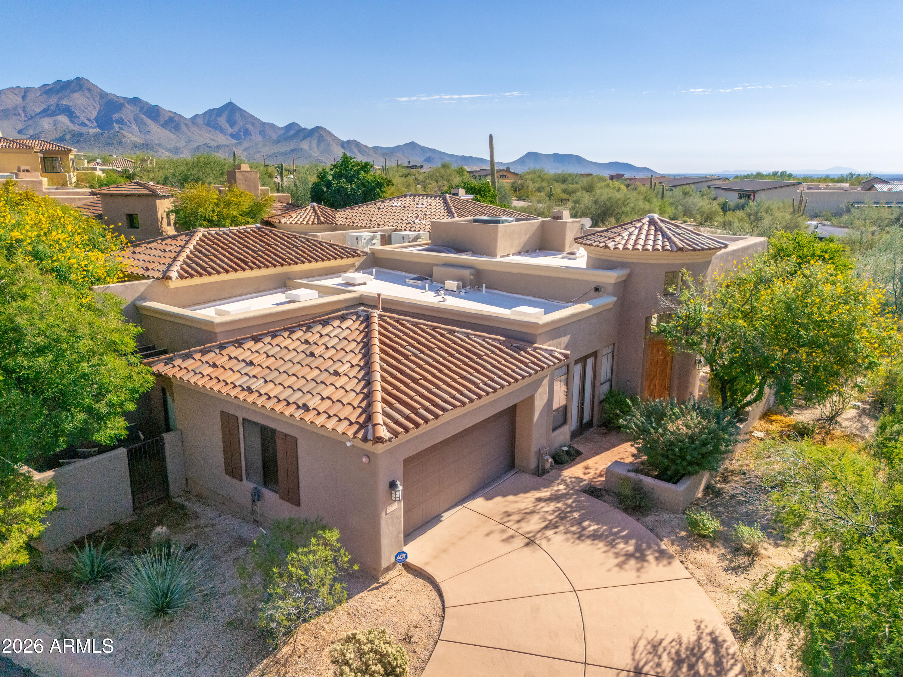 Aerial view of a tile-roofed Southwestern home with desert landscaping and mountains behind it.