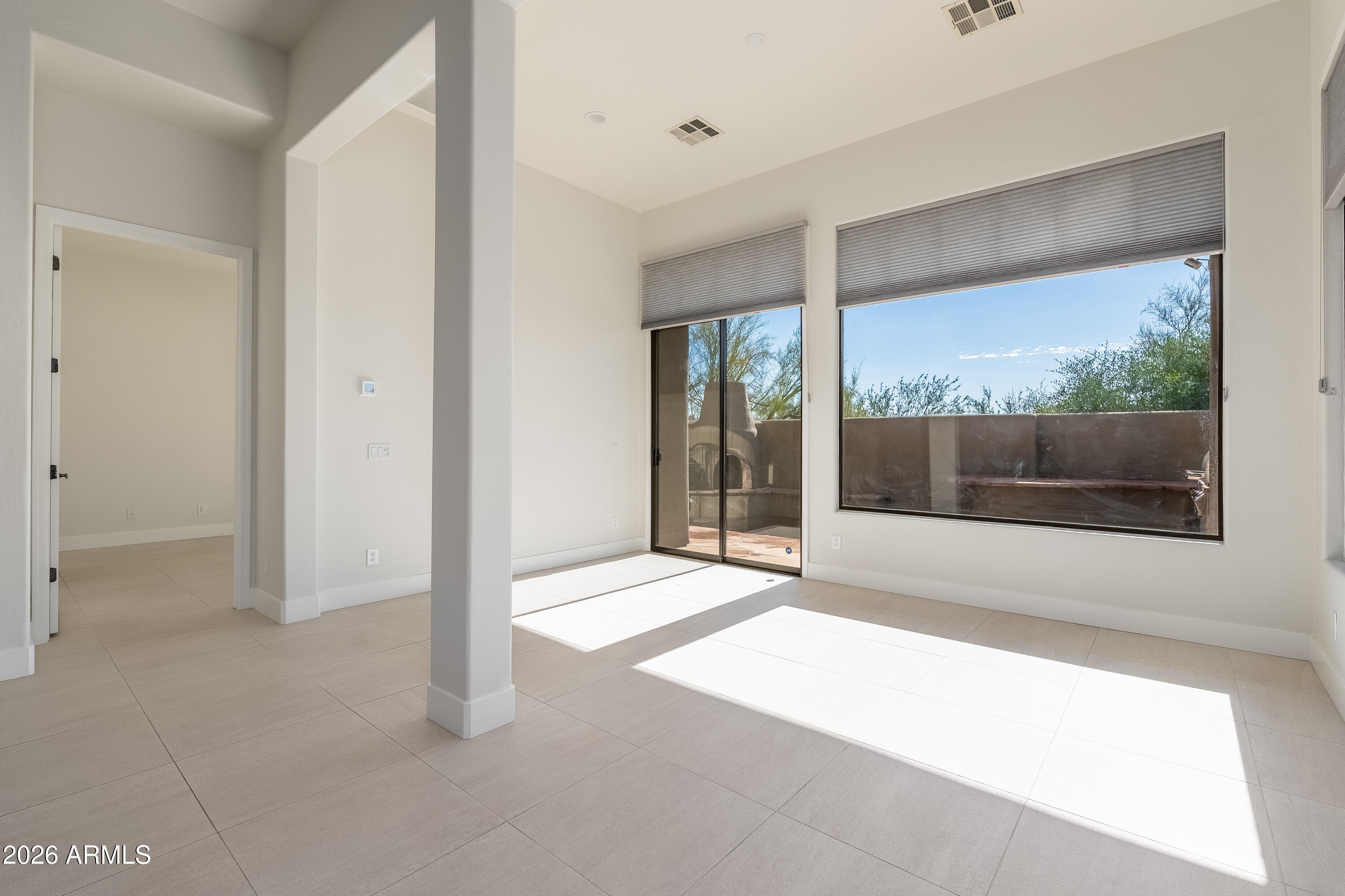 Vacant tiled room with large windows and a sliding glass door opening to a walled patio.