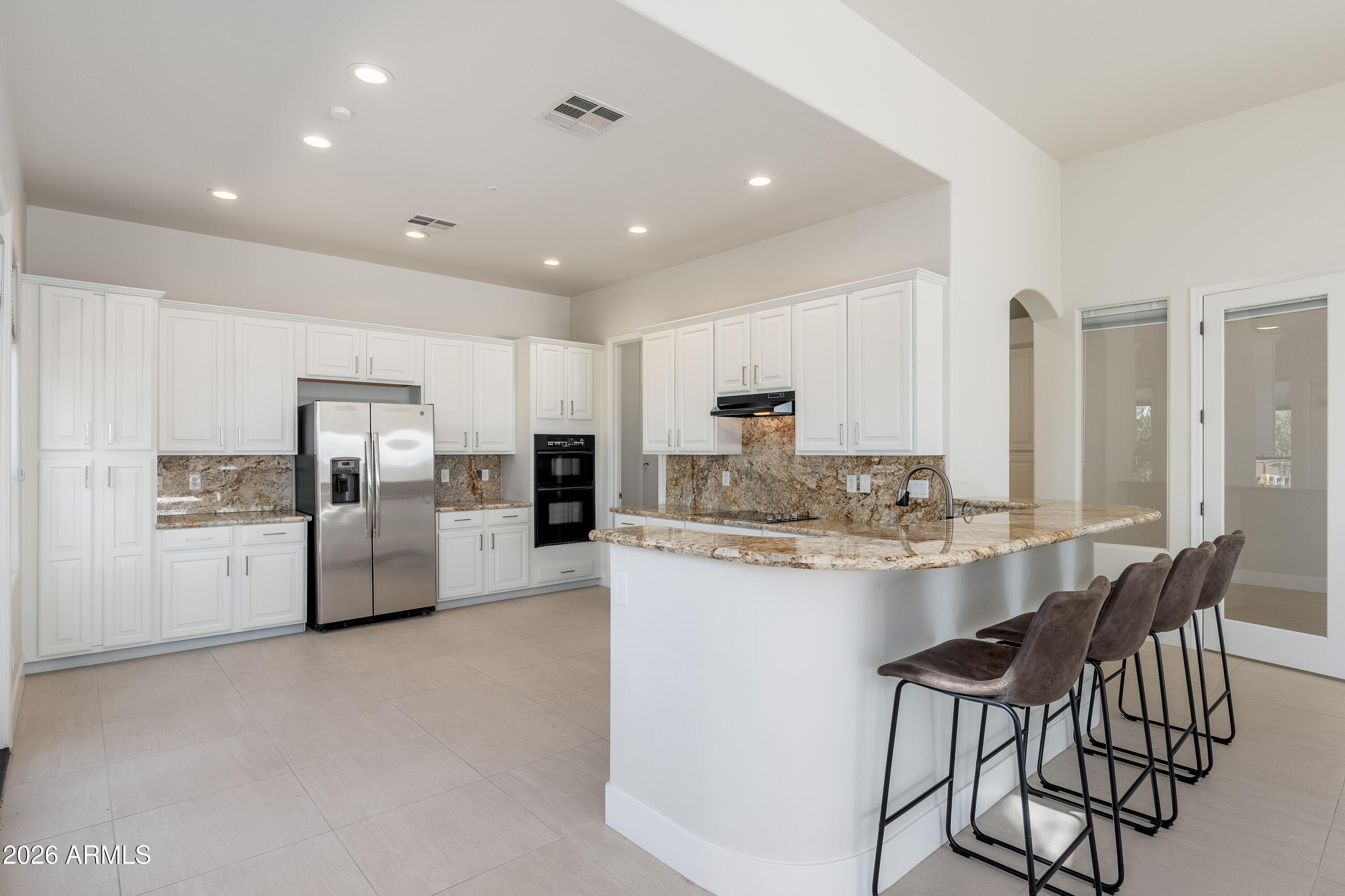 Kitchen with white cabinets, granite counters, stainless appliances, and a curved island with bar stools.