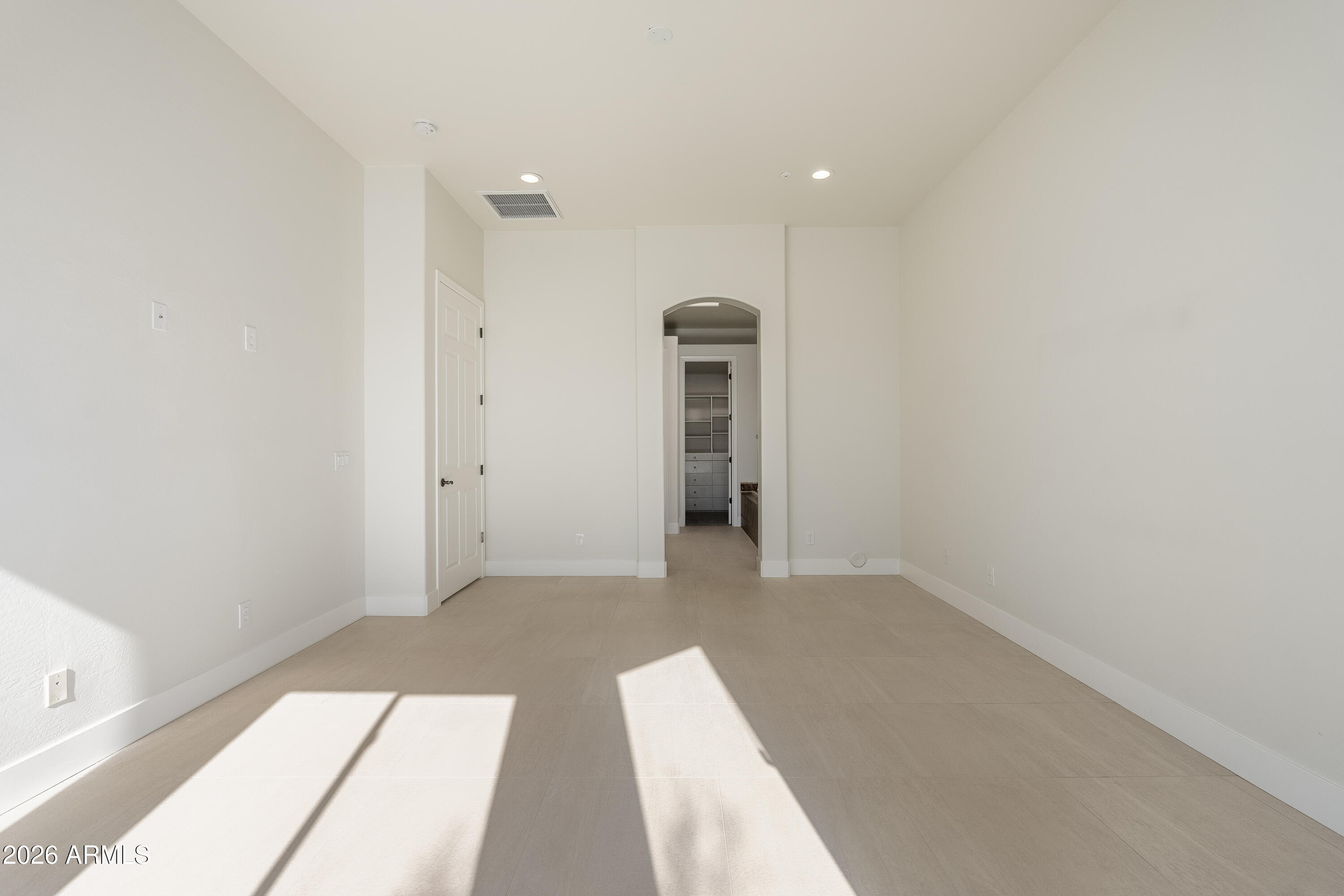 Vacant bright room with tiled floors, an arched doorway, and sunlight streaming across the floor.