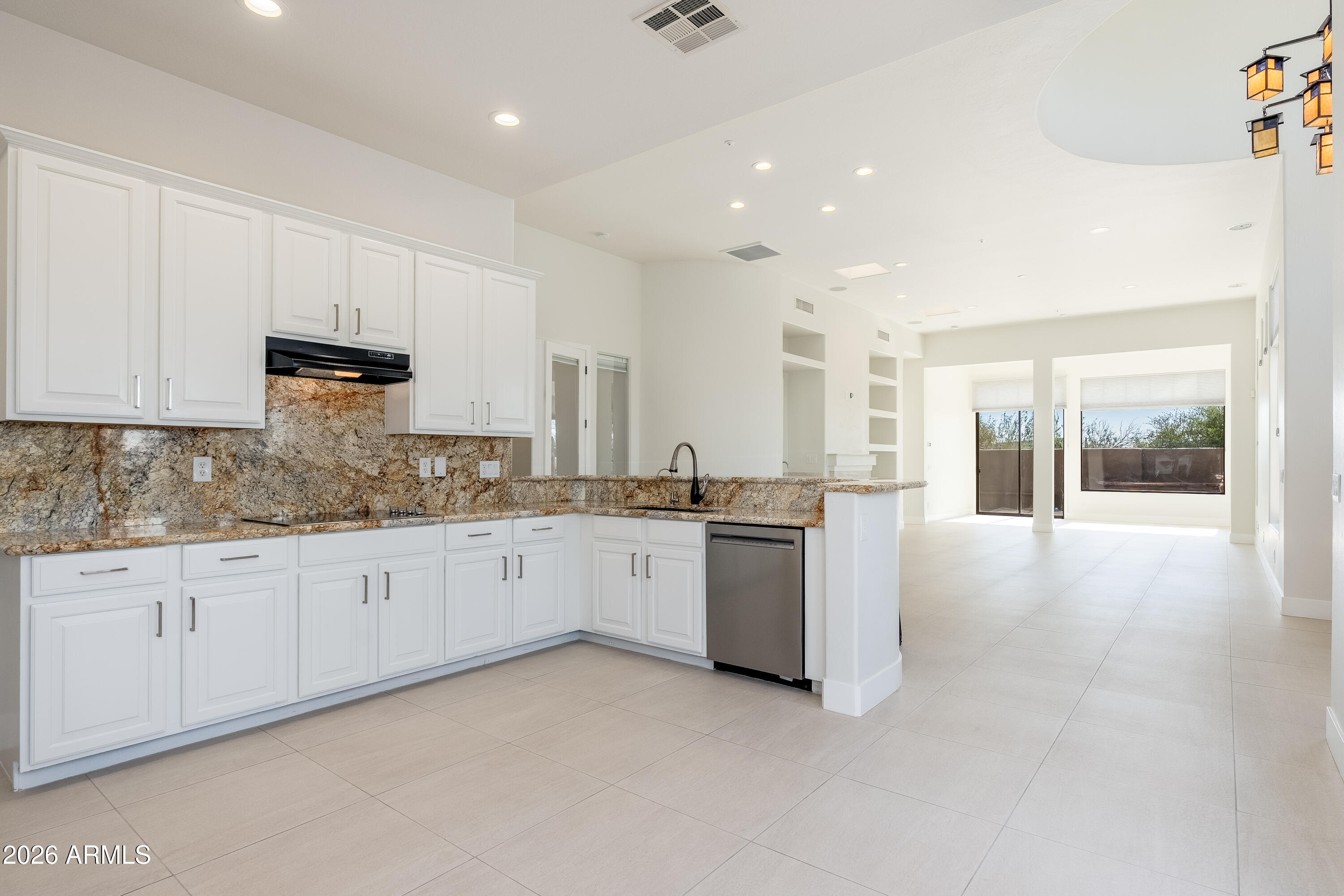 Kitchen with white cabinets and granite counters opening to a bright, tiled living area.