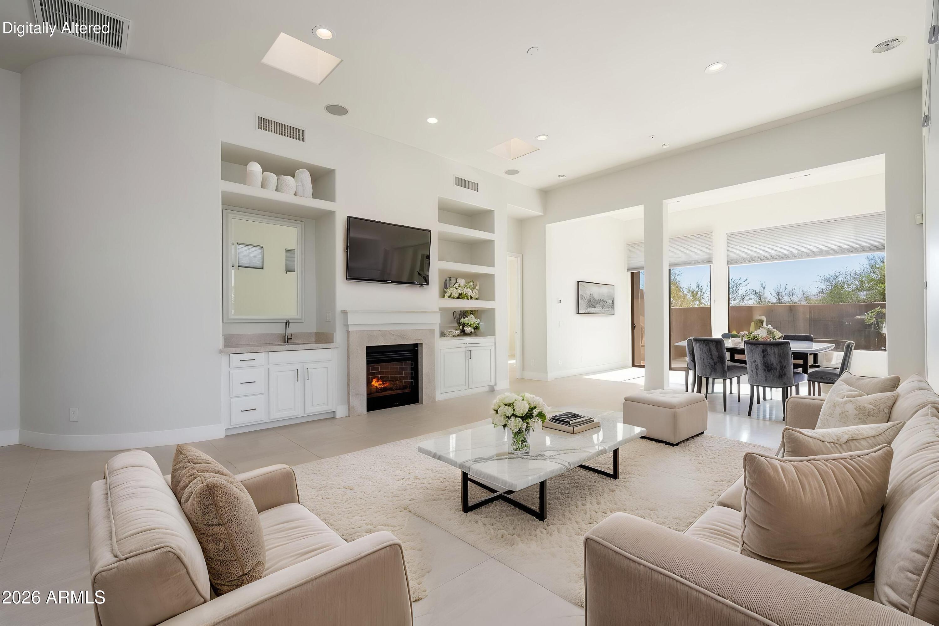 Staged living room with cream sofas, a fireplace, built-in shelves and large windows opening toward a patio.