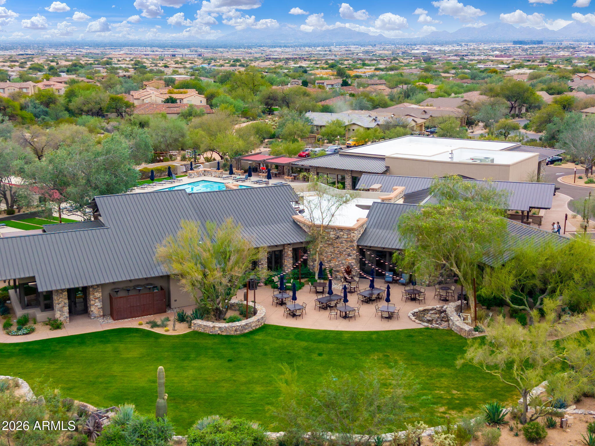 Community clubhouse with a swimming pool, furnished patio, and landscaped lawn, with mountains in the distance.