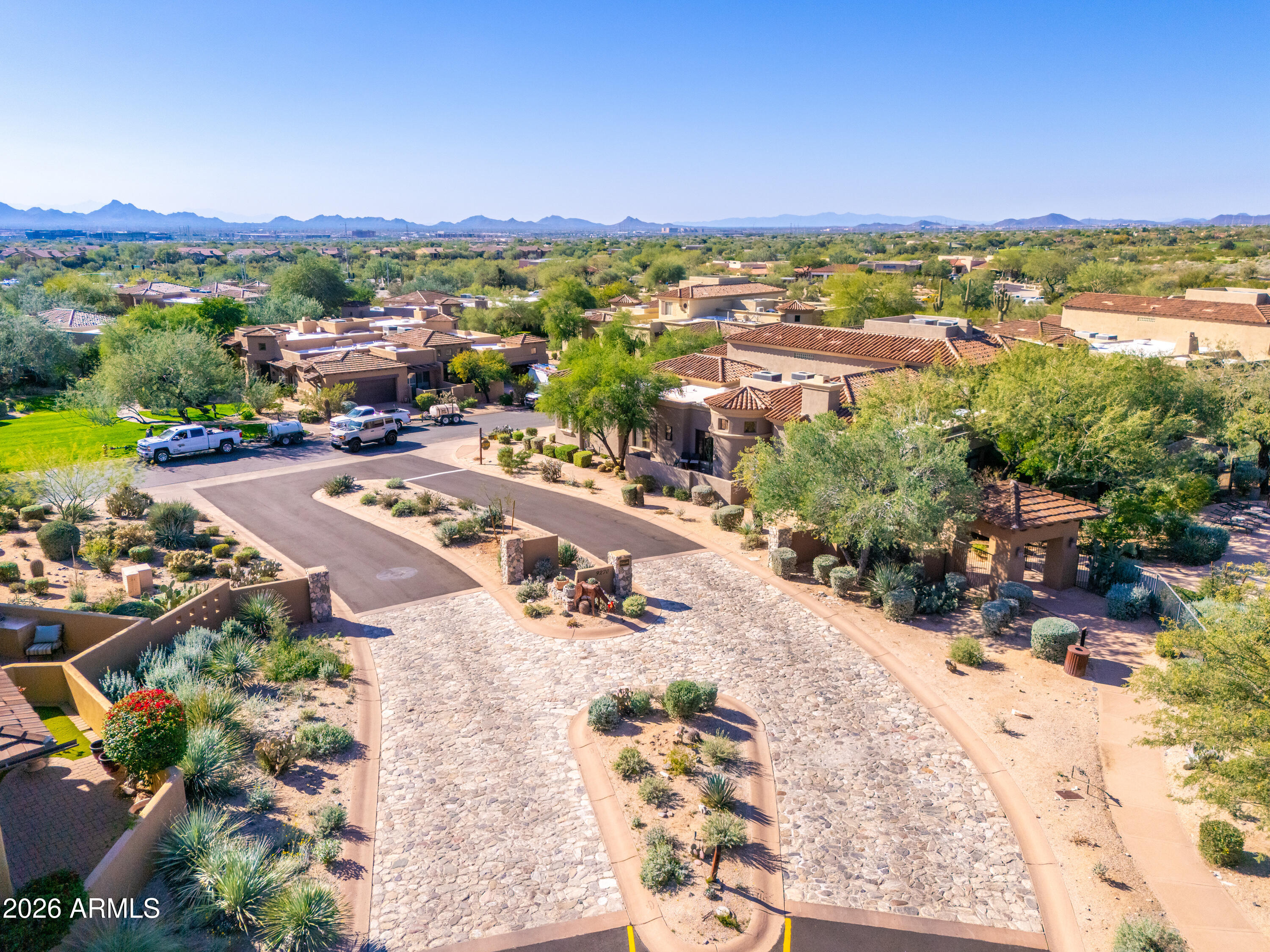 Aerial view of a desert community with a stone-paved entrance, tile-roof homes, and distant mountains.