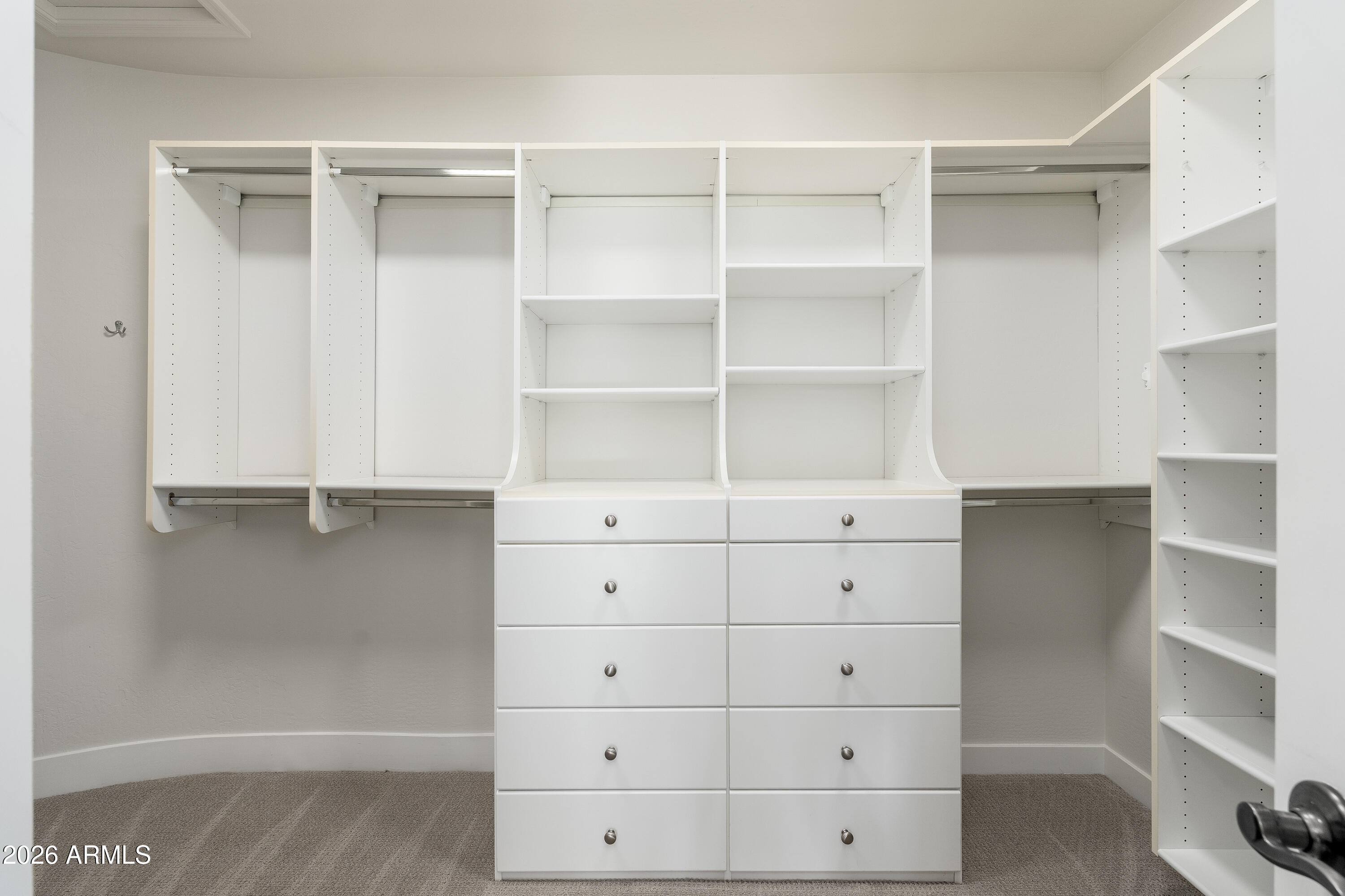 Walk-in closet with white built-in shelving, hanging rods, and a central chest of drawers.
