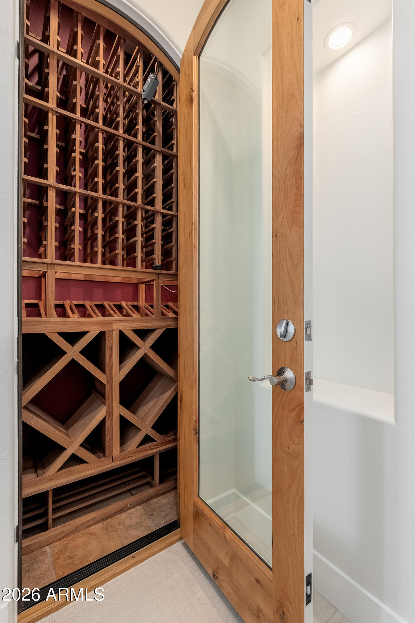 Wine cellar with wooden wine racks and an open glass door.