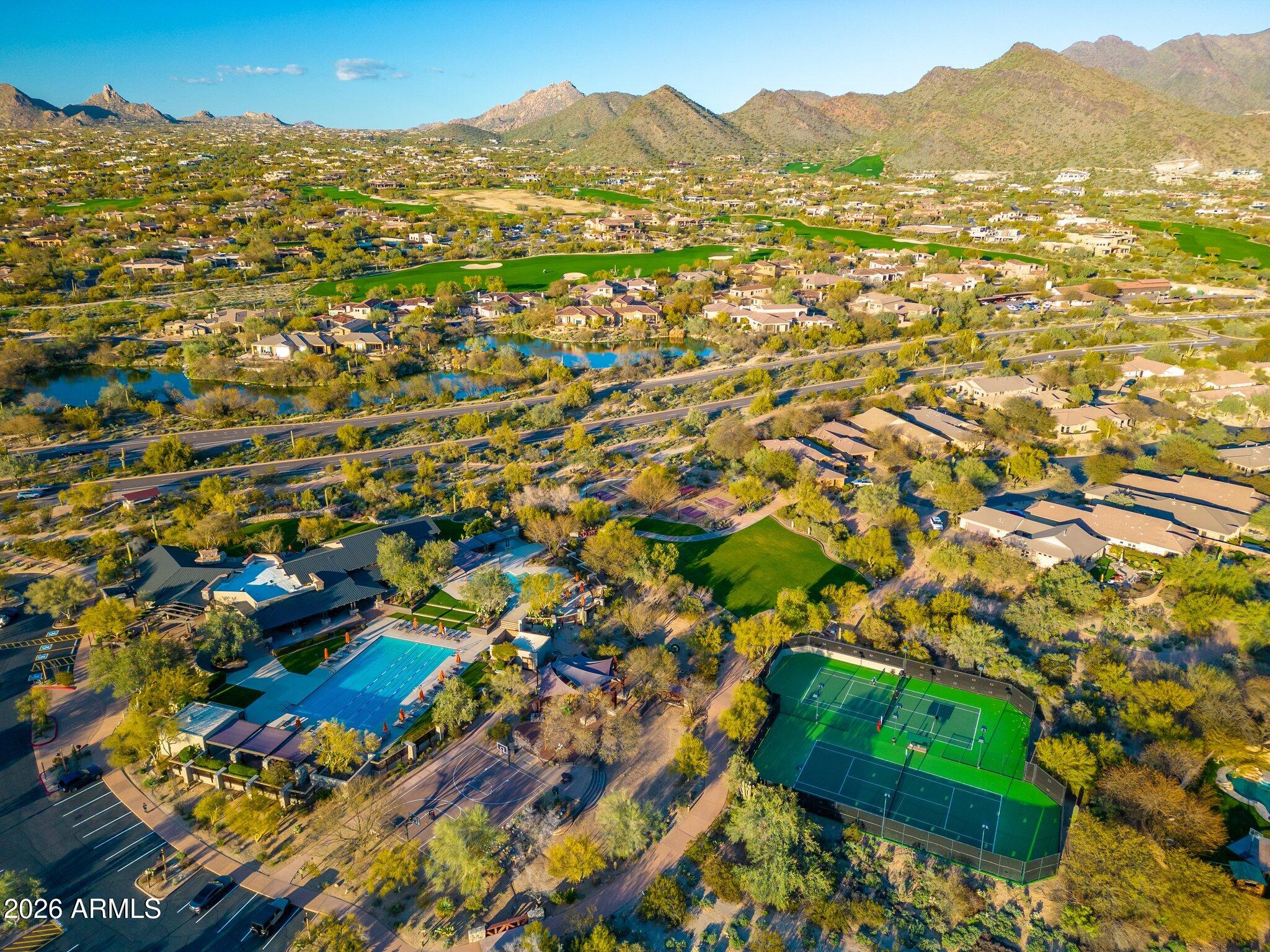 Aerial view of a Scottsdale community with a pool, tennis courts, homes, and desert mountains.