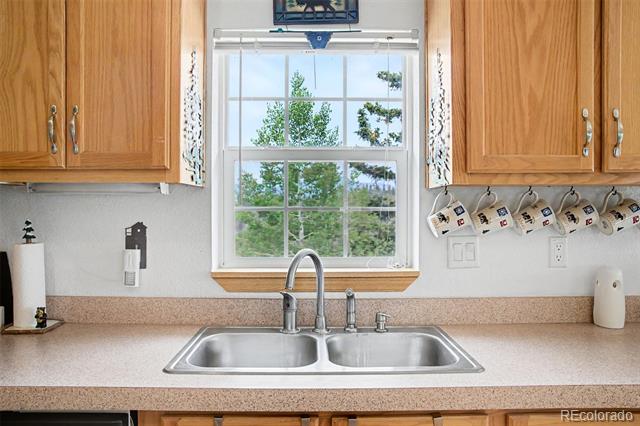 Kitchen sink beneath a large window, with wood cabinets and a view of trees.